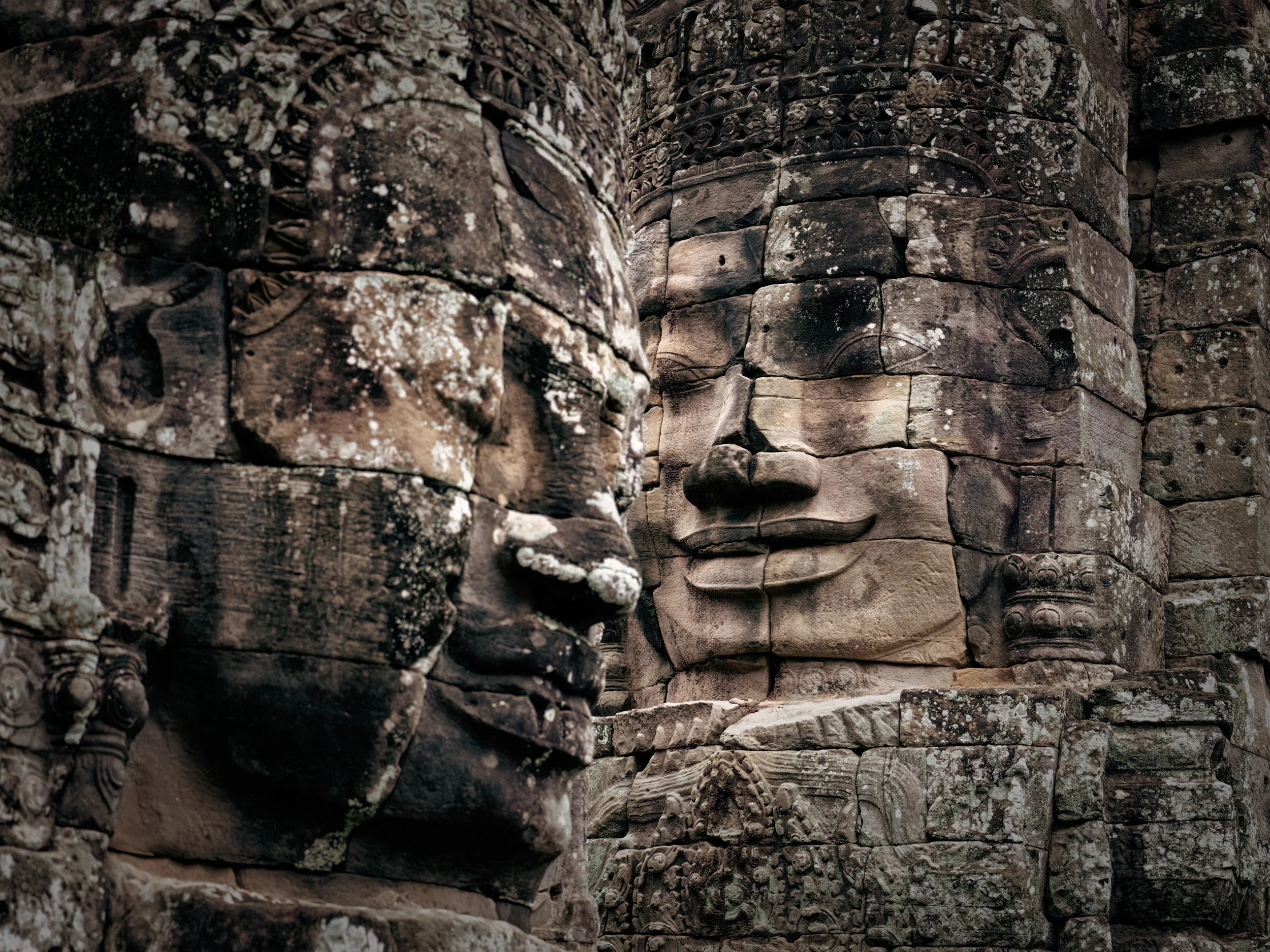 Ancient Bayon temple stone face carved into weathered ruins at Angkor, Cambodia.