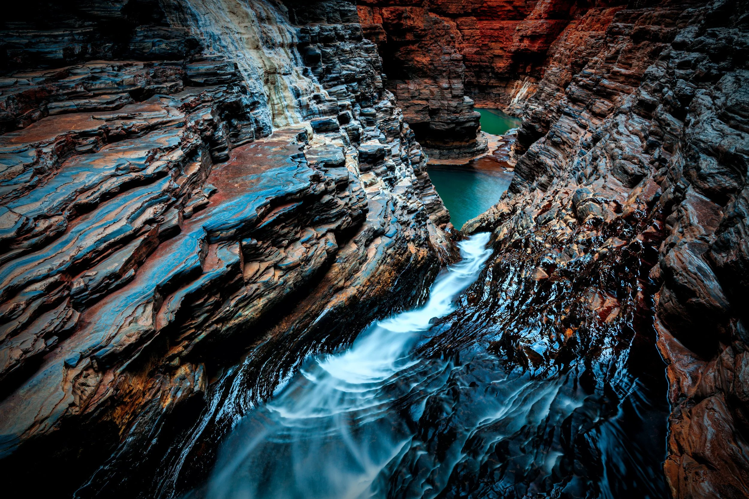 Turquoise water rushing through Regans Pool in Hancock Gorge, Karijini National Park, surrounded by dramatic red and blue rock walls.