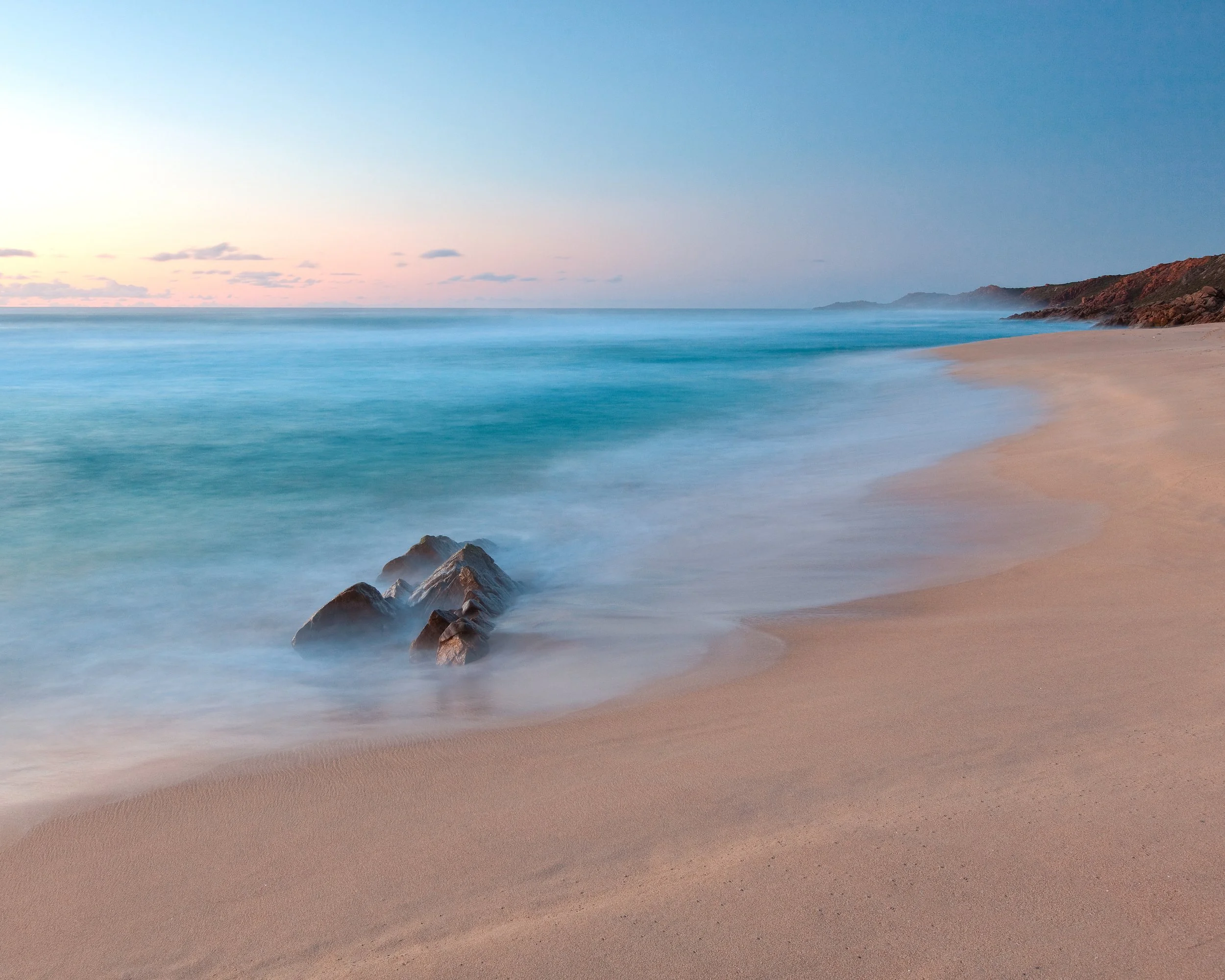 Soft turquoise water and pale sand at Injidup Beach near Margaret River, Western Australia, with a lone rock in the calm shoreline surf.