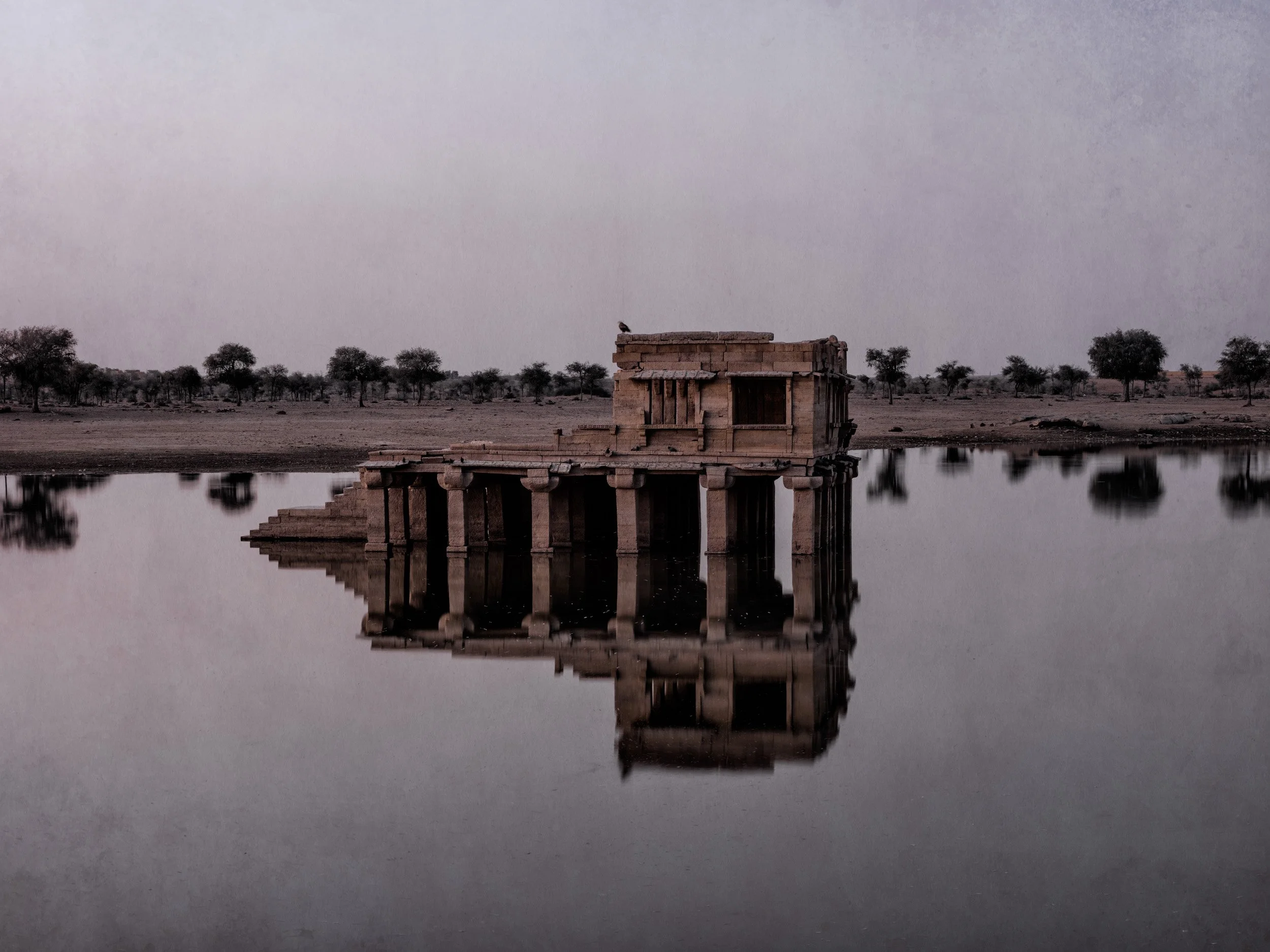 Subdued minimalistic view of a ruined palace pavilion reflected in a still lake in India.