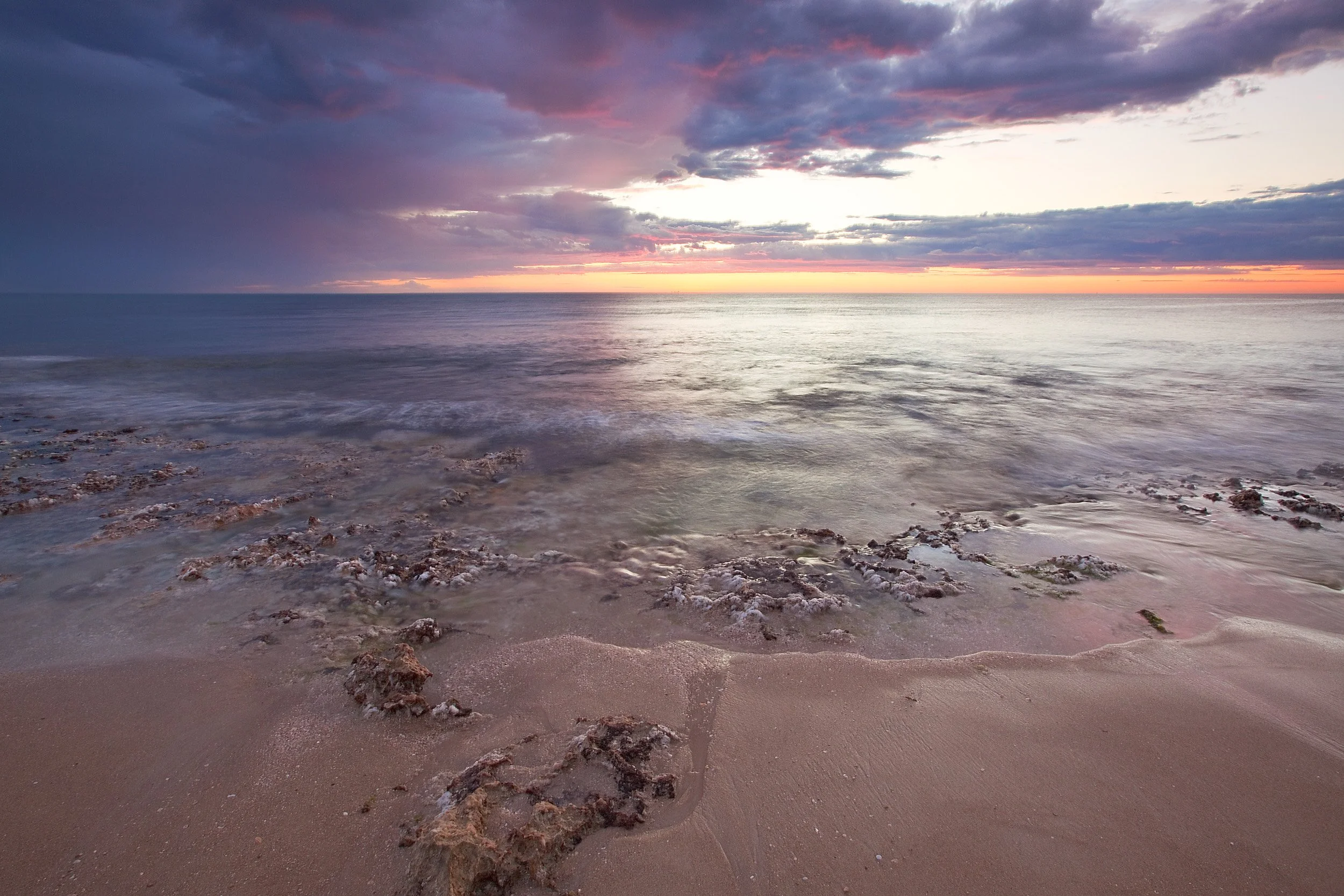 Perth coastal rock platform at sunset with reflective tide pools, purple sky, and calm ocean horizon.