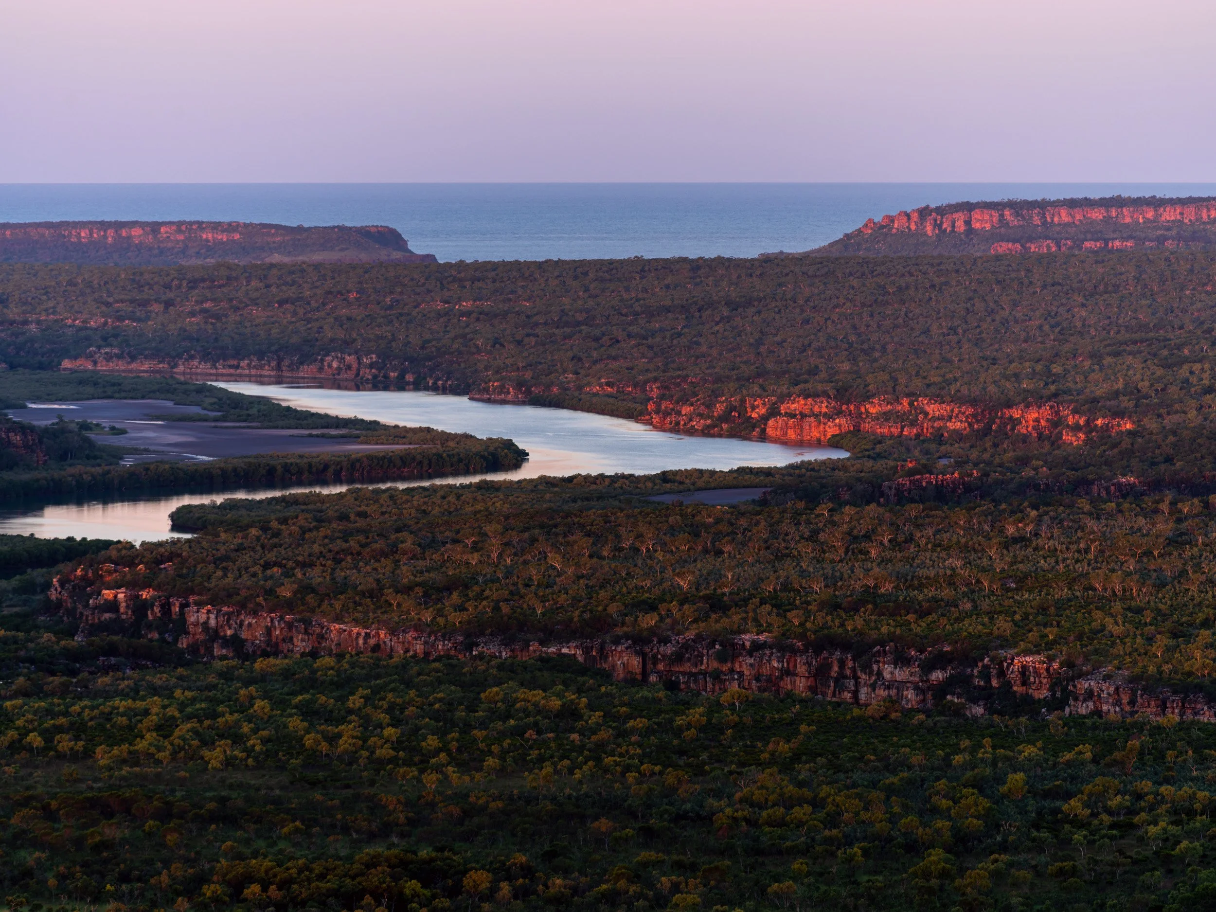 Kimberley river and red escarpment at sunset in Western Australia, with soft purple sky and remote outback wilderness.