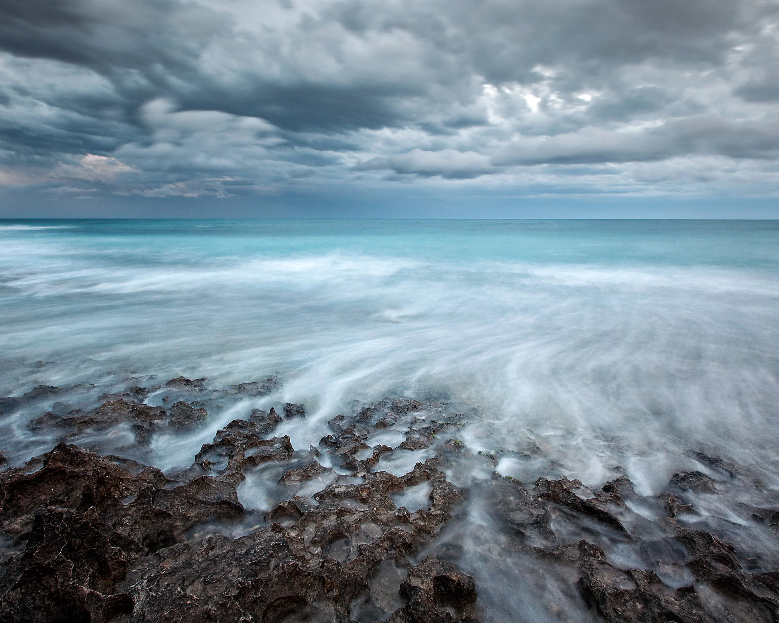 Stormy North Beach seascape in Perth with turquoise ocean, dark rocks, and moody coastal clouds.