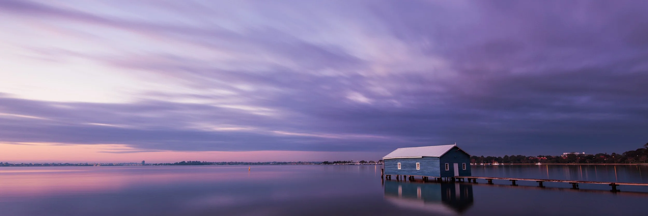 Crawley Boatshed on Matilda Bay in Perth at dusk, reflected in calm water under a purple and blue evening sky.