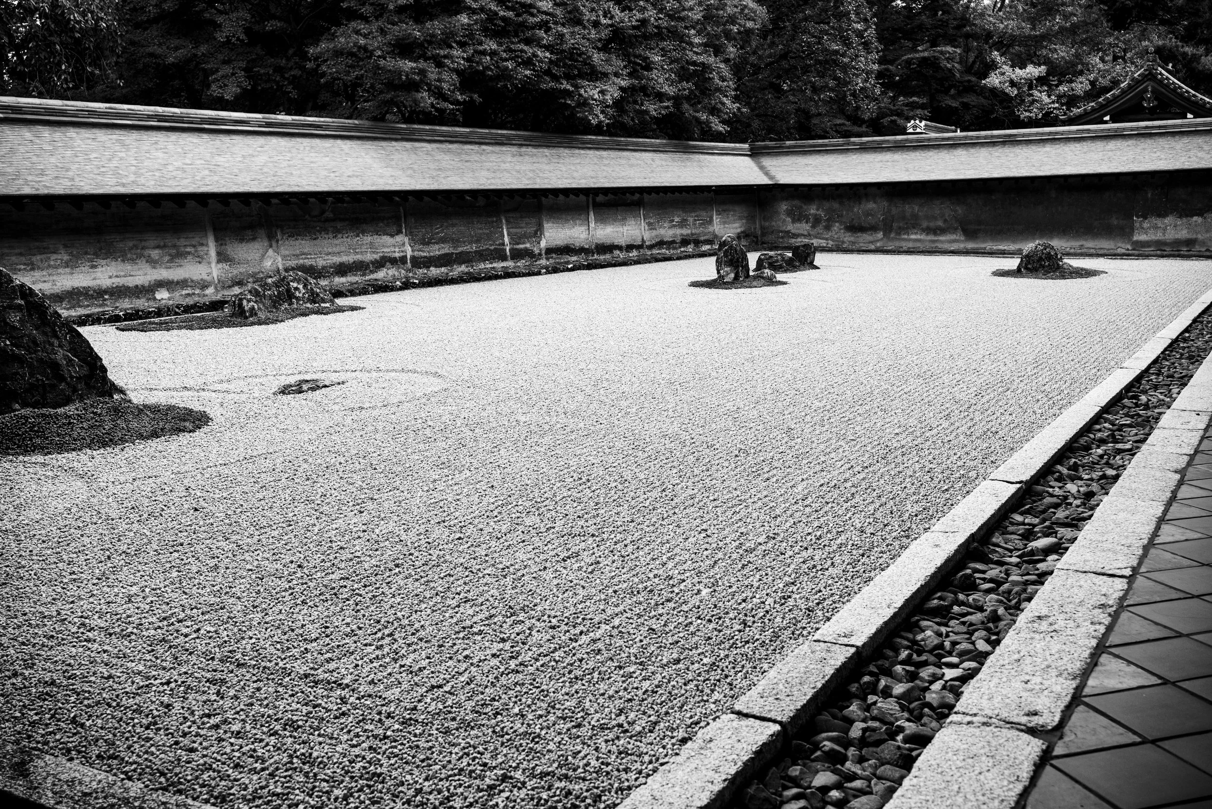 Black and white Zen rock garden with raked gravel and temple roof detail in Kyoto, Japan.