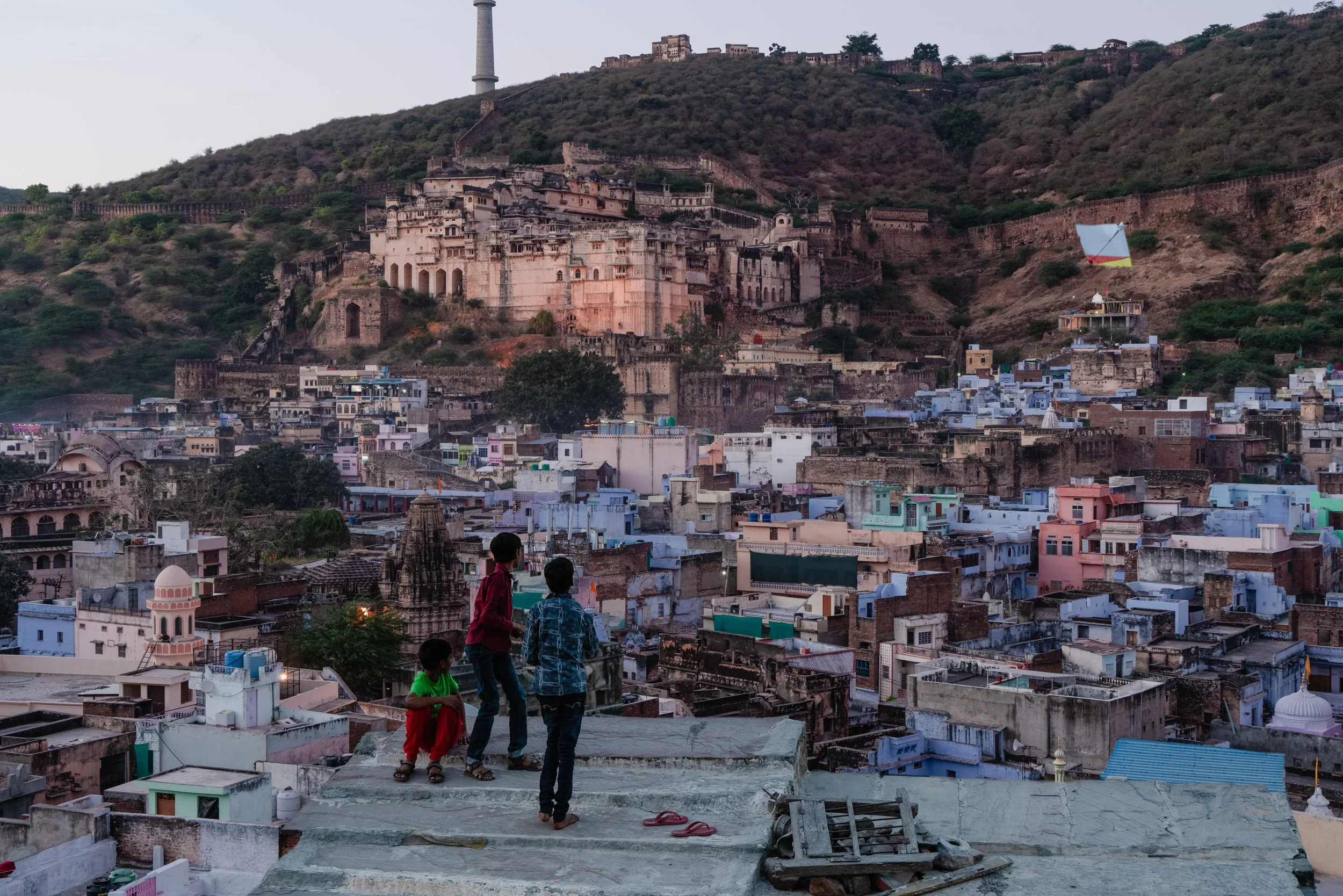 Bundi cityscape in Rajasthan with blue houses, hillside palace, and three children overlooking the town.