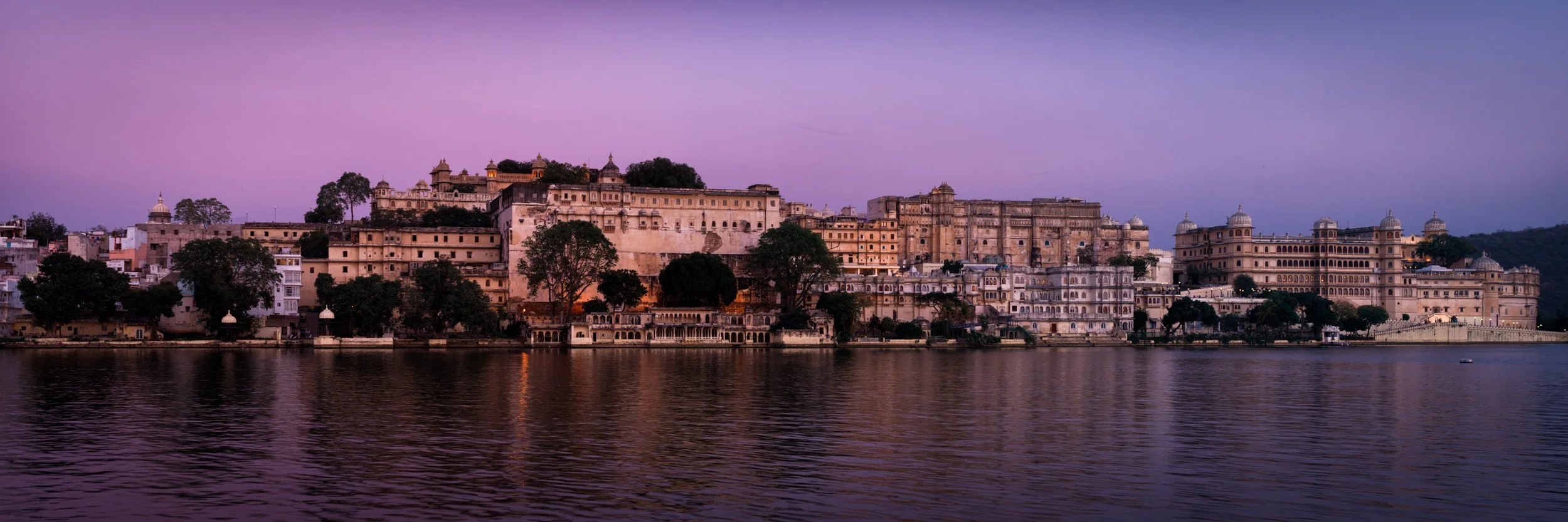 Udaipur Lake Pichola panorama at dusk, with palace architecture, purple sky, and calm lake reflections in Rajasthan, India.