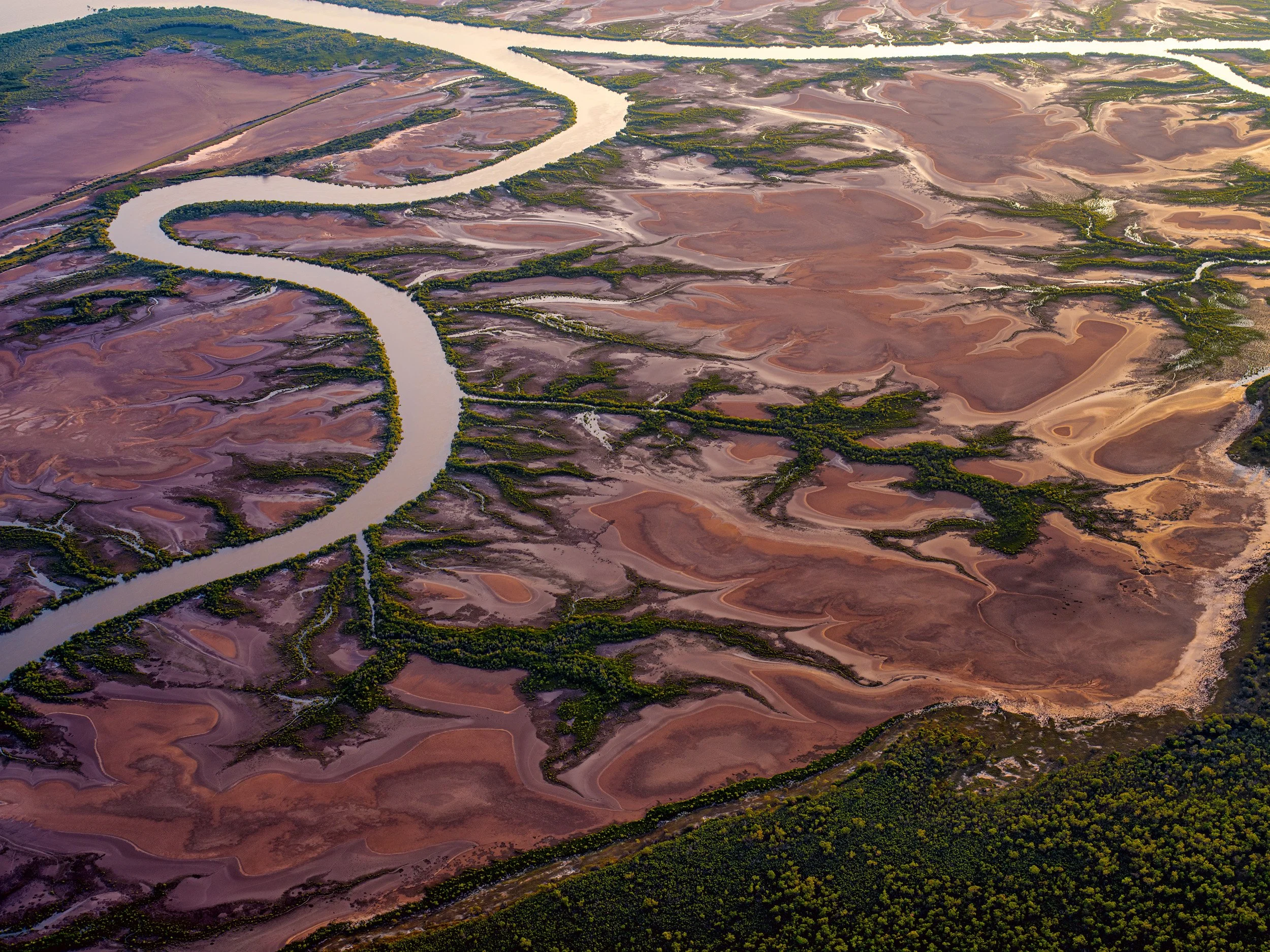 Aerial landscape of a meandering river through Kimberley tidal flats and remote outback wetlands in Western Australia.