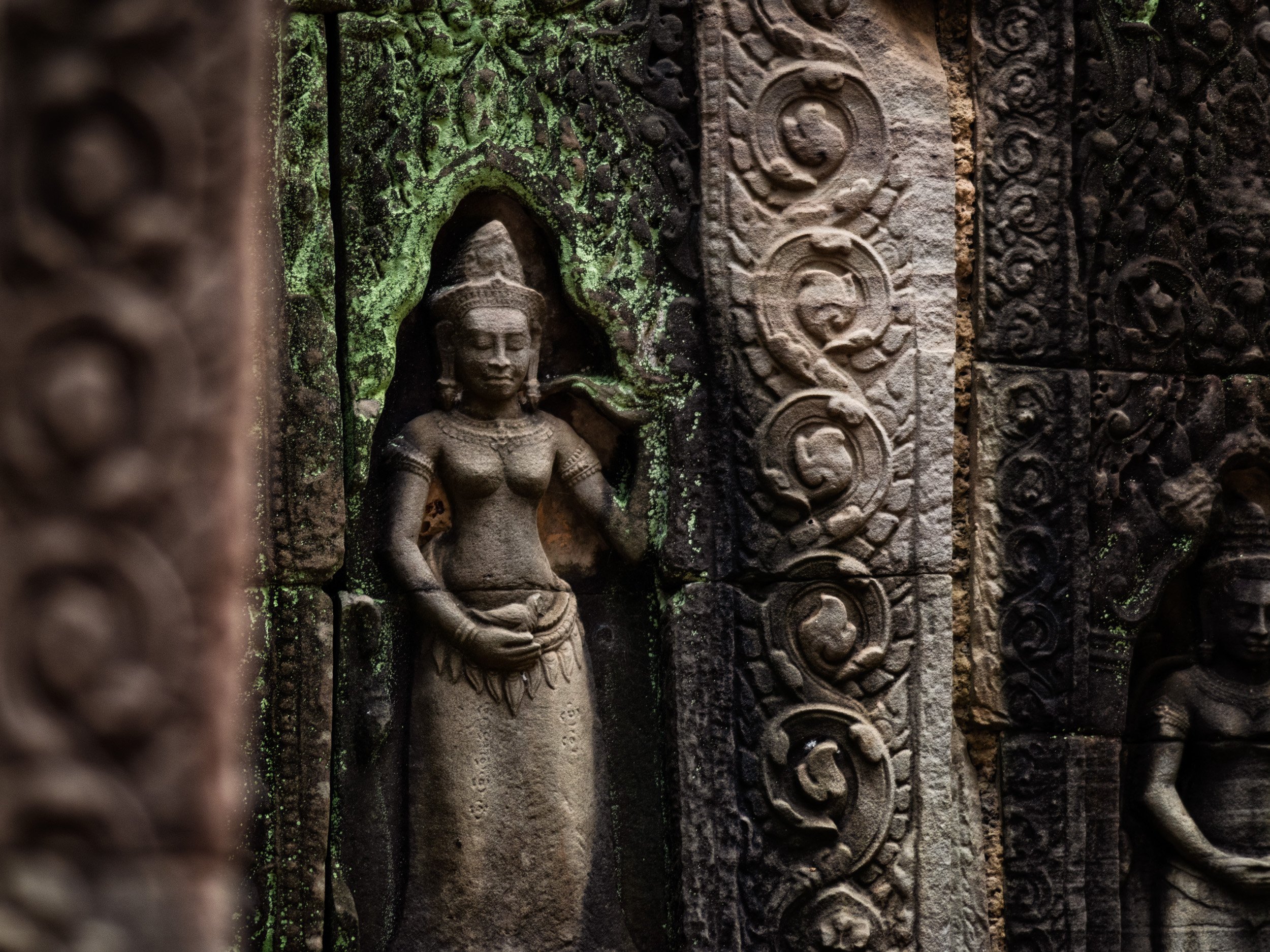 Khmer devata statue carved into an ancient Angkor temple wall, surrounded by ornate stone details.