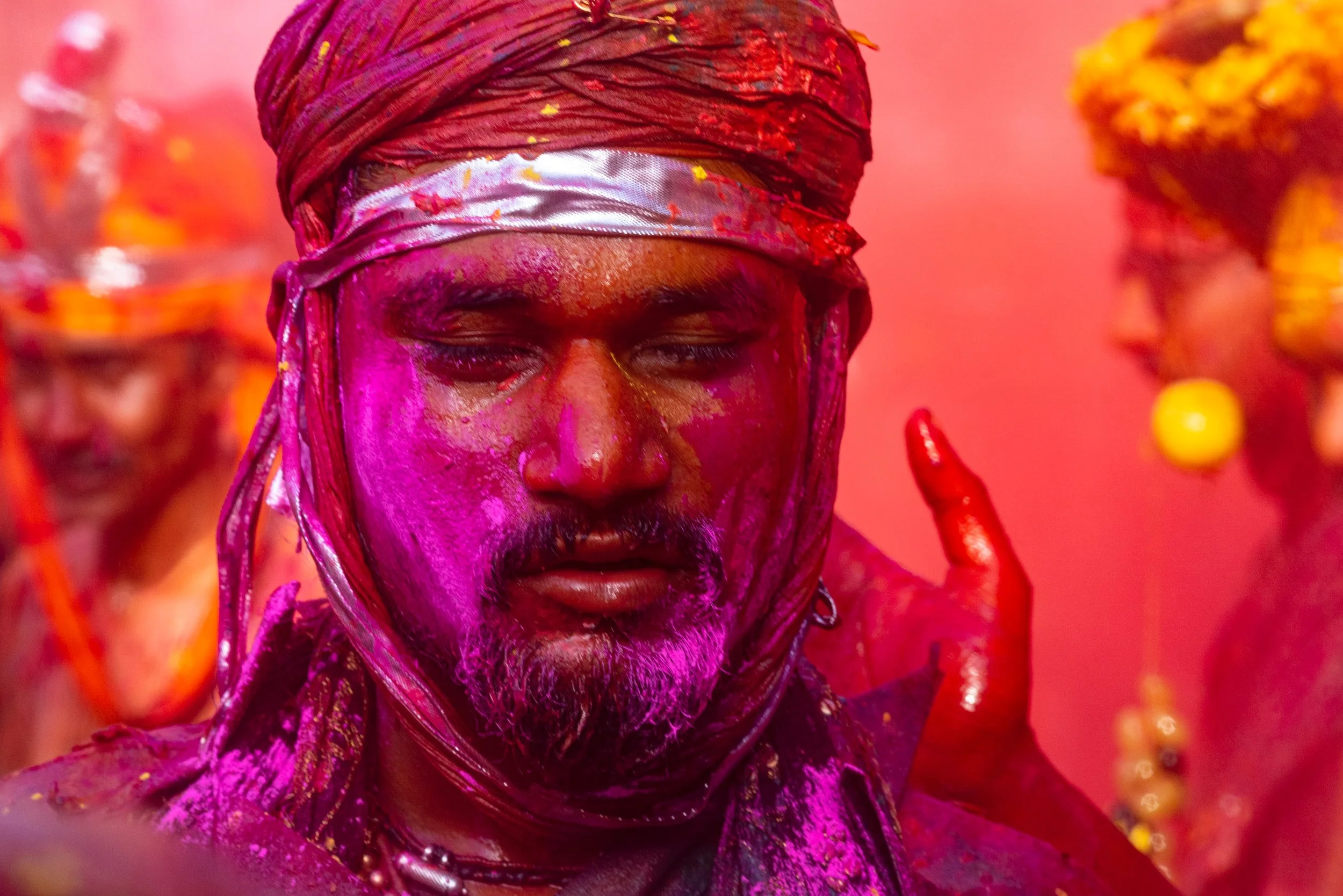 Close portrait of a man covered in vivid purple and red Holi powder, wearing a headscarf during a lively Indian color festival.