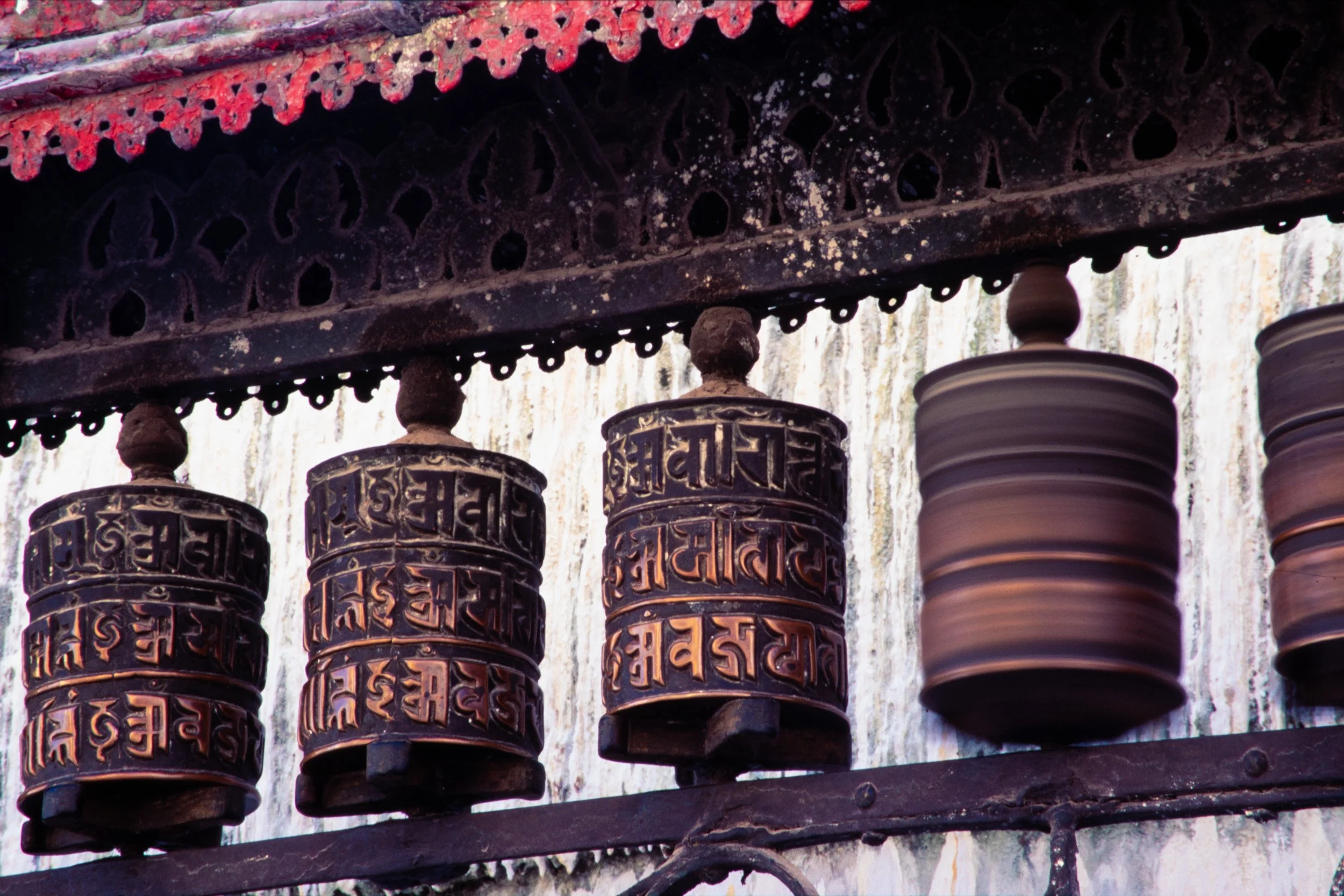 Tibetan Buddhist prayer wheels lined up inside a Nepalese temple corridor.