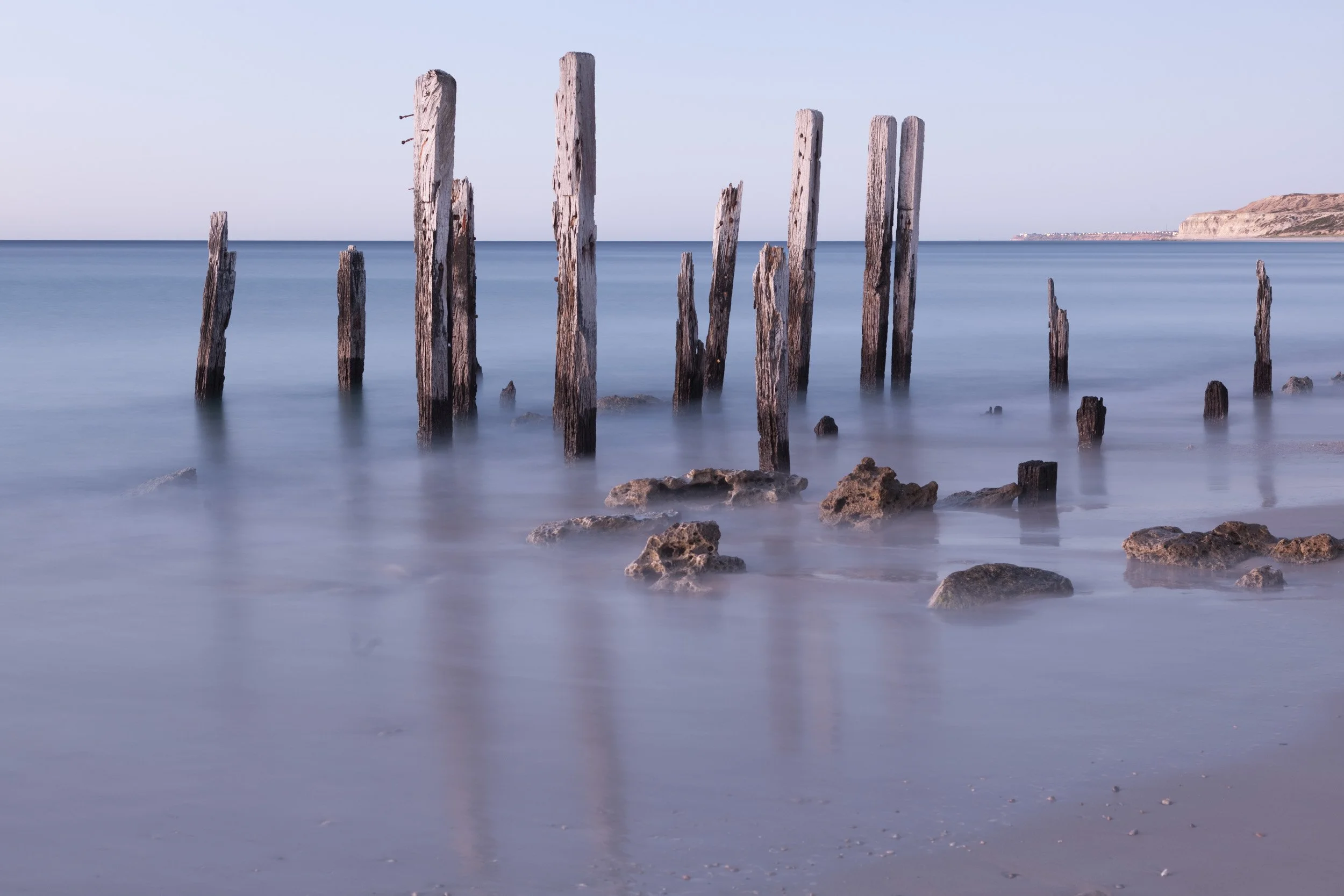 Port Willunga jetty pylons in South Australia captured as a long exposure, with weathered wooden posts standing in smooth blue water.