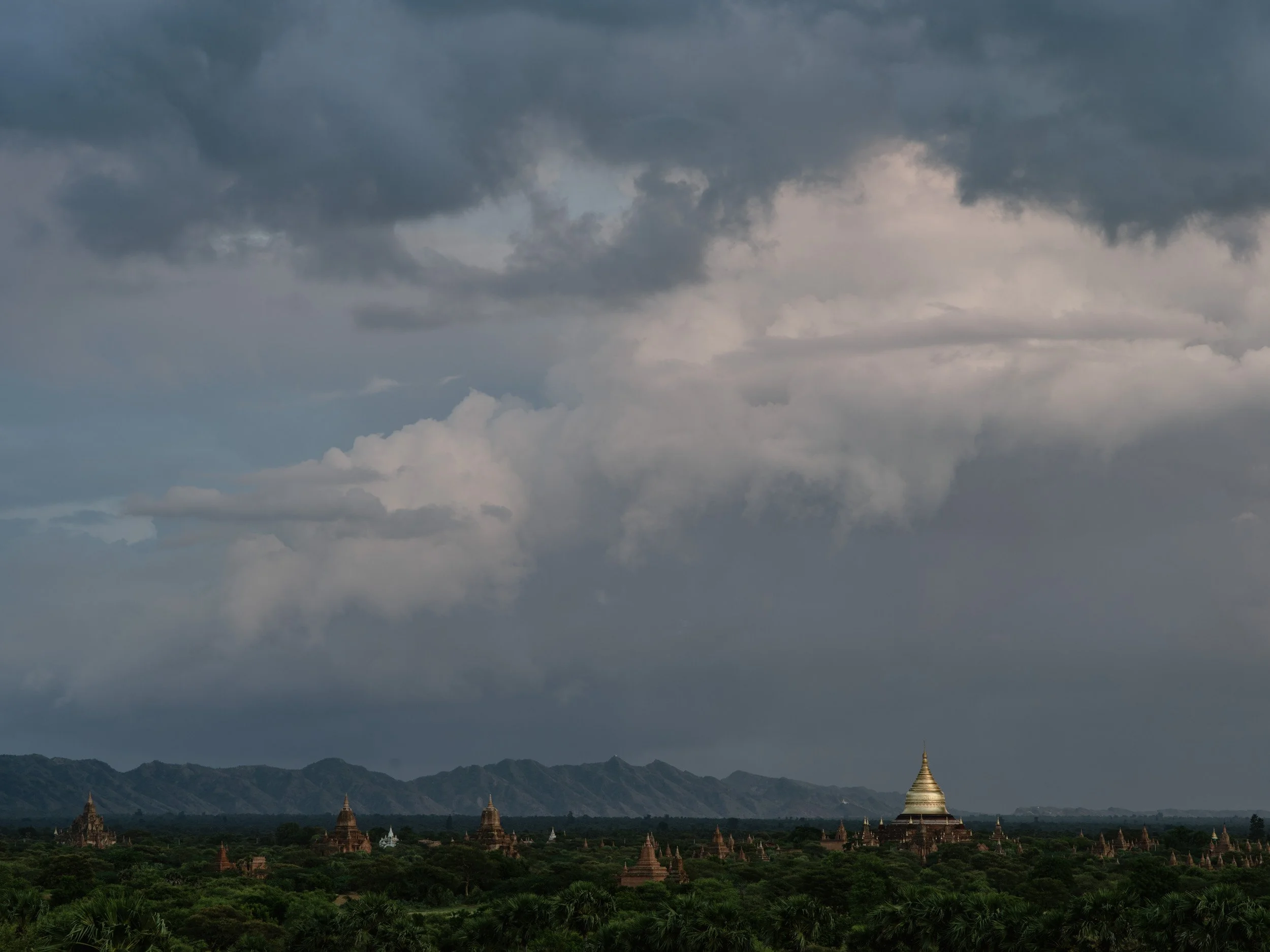 Dramatic storm clouds over the Bagan plains with a small golden pagoda in Myanmar.
