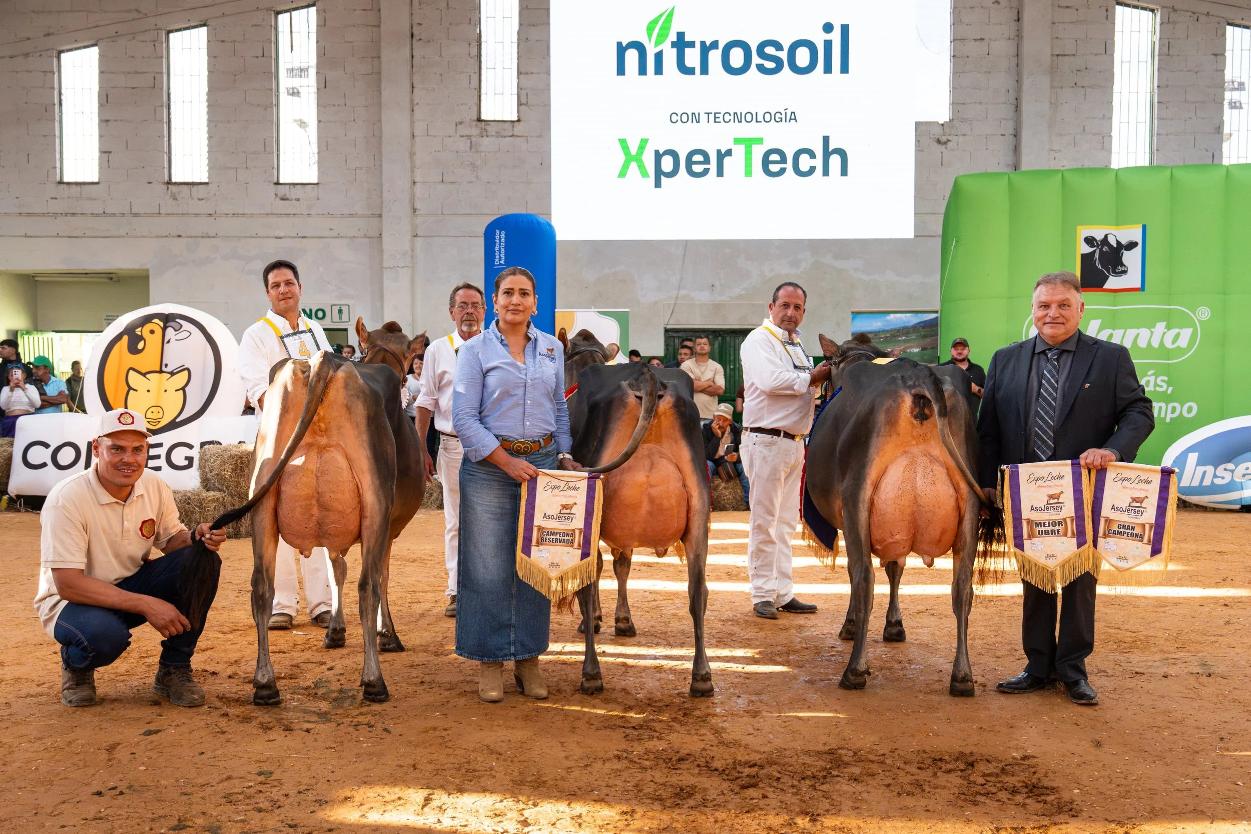 People posing with prize-winning dairy cows at a Colombian livestock show surrounded by ExpoLeche and agricultural sponsor banners