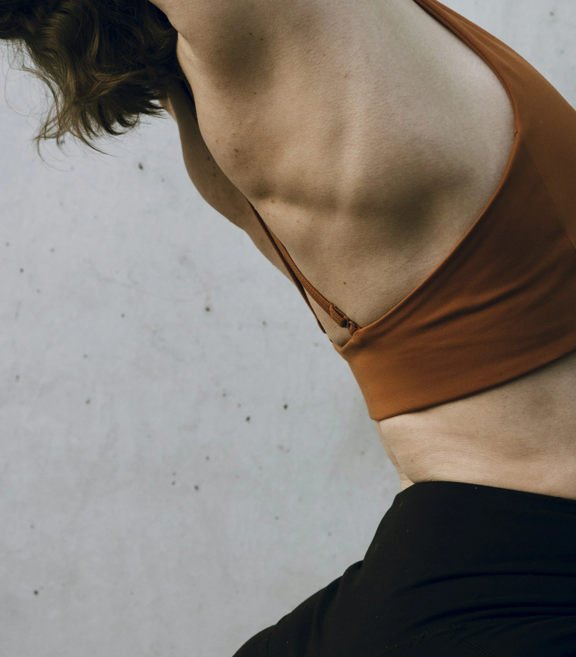 Close-up of a woman's upper body wearing a brown sports bra and black athletic pants, with a neutral background.