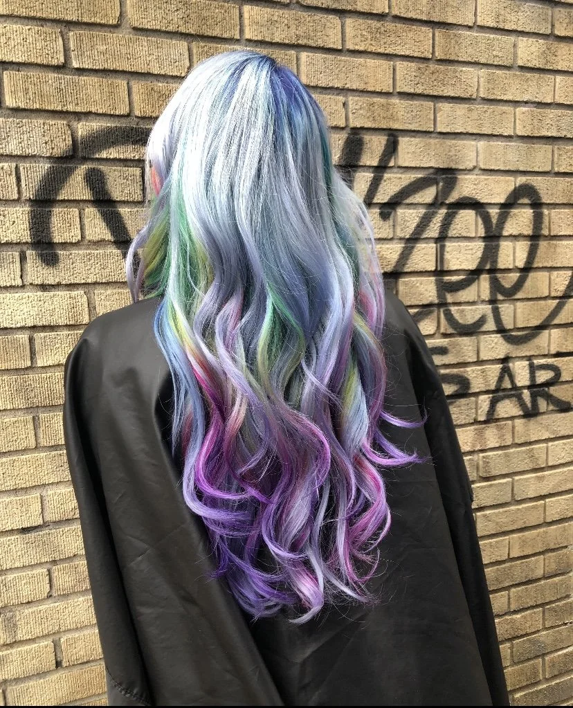 Long pastel rainbow-toned hair with waves against brick wall