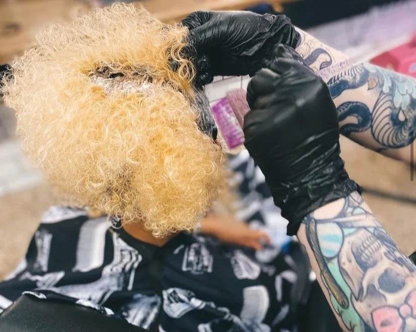 Curly hair being bleached with gloved hands