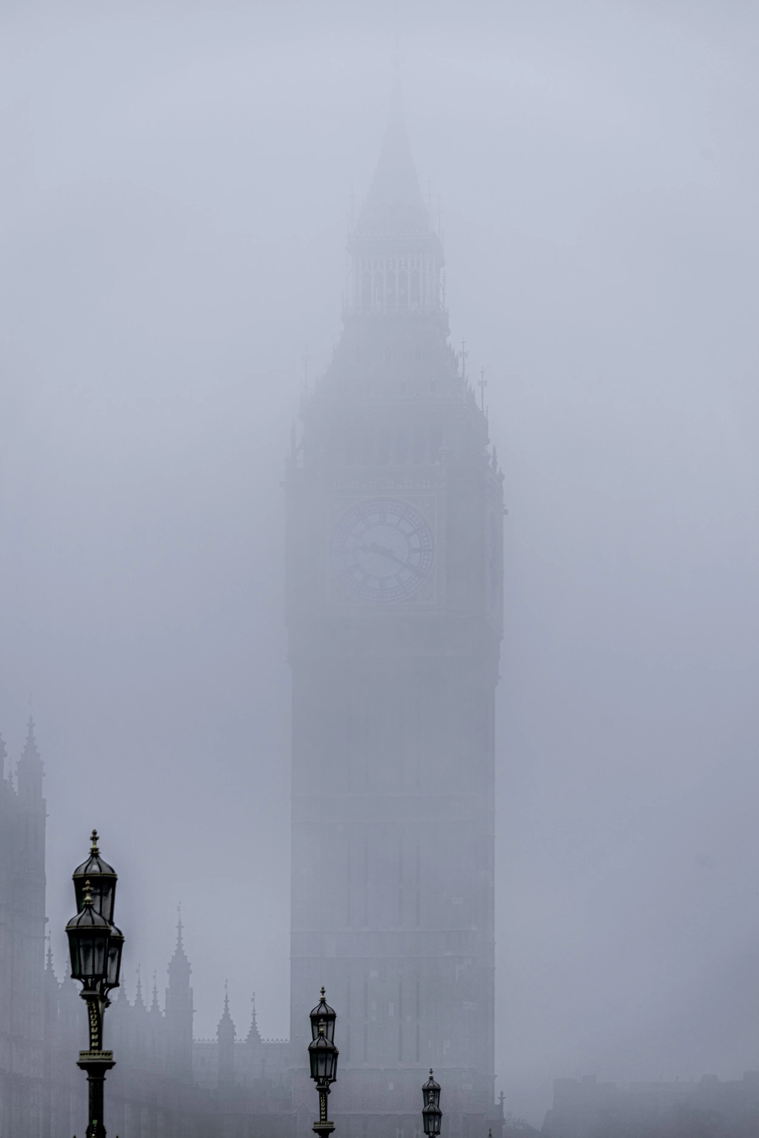 Foggy view of Elizabeth Tower in London with visible street lamps.