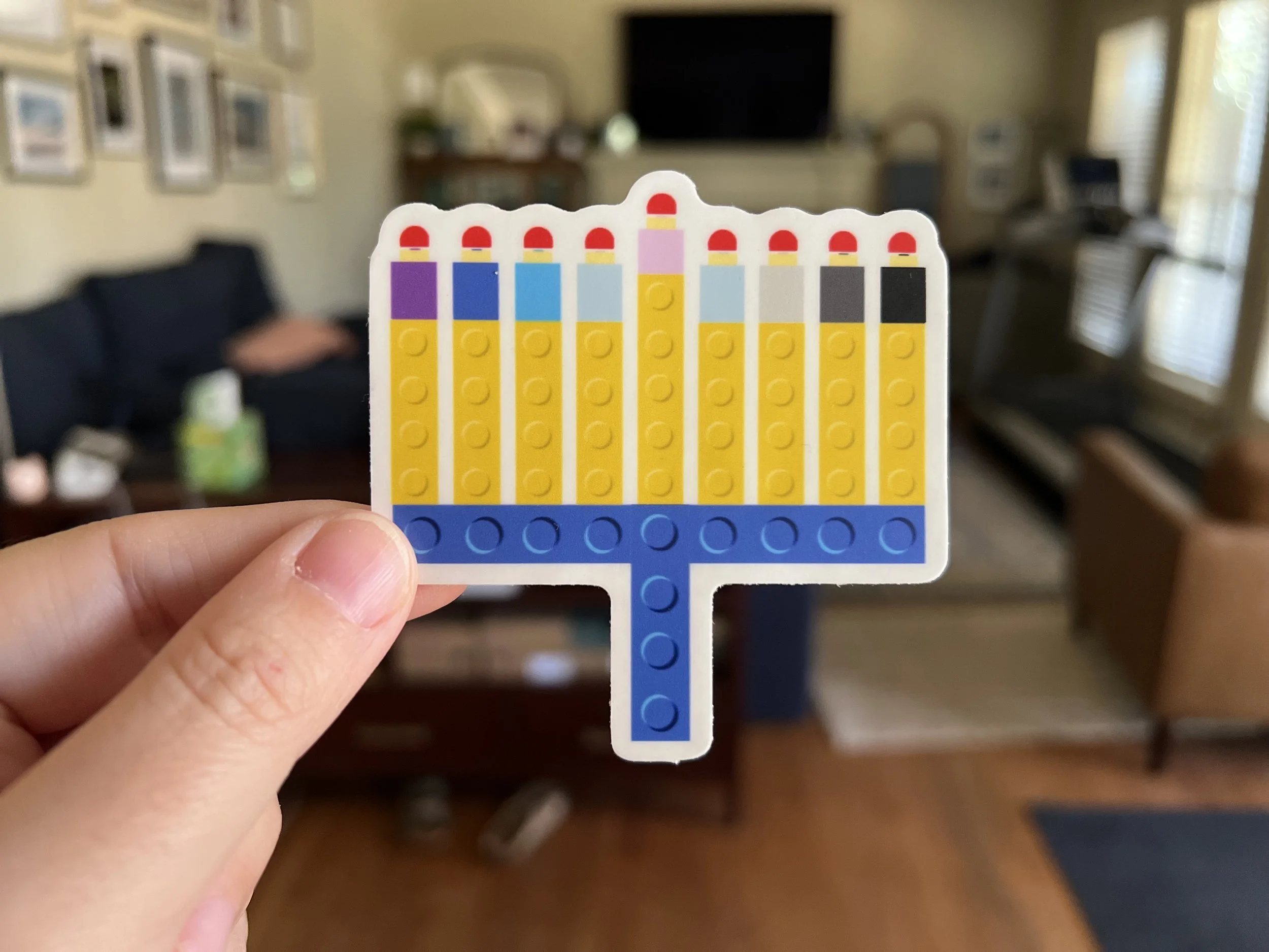 Hand holding a sticker of a menorah made from colorful toy building bricks.