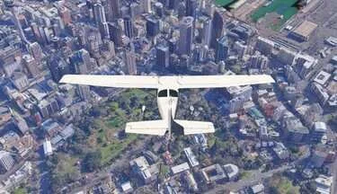 A white airplane flying above a dense city with tall buildings and a park below.
