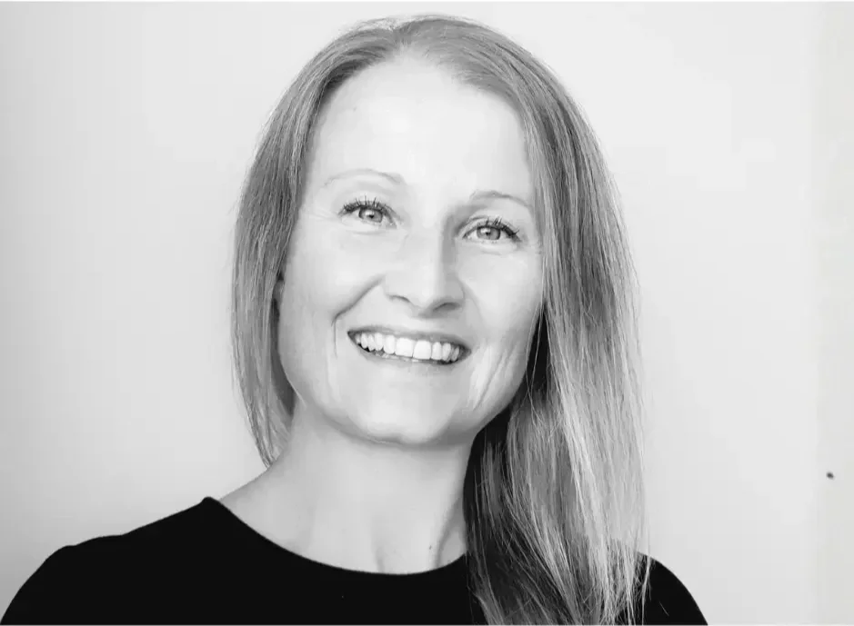 Black and white portrait of a woman with long, straight hair, smiling at the camera, wearing a black top against a plain background.