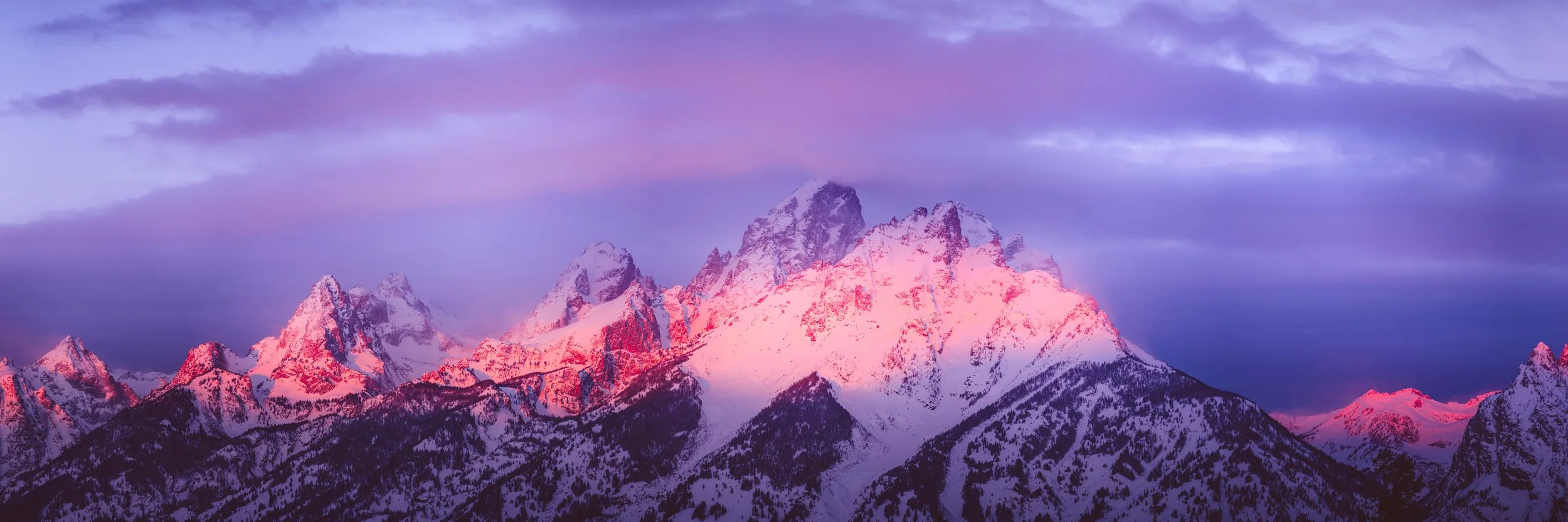 Snow-covered Grand Teton mountains at sunrise in Winter with a pink and purple sky. By Archie Carmel.