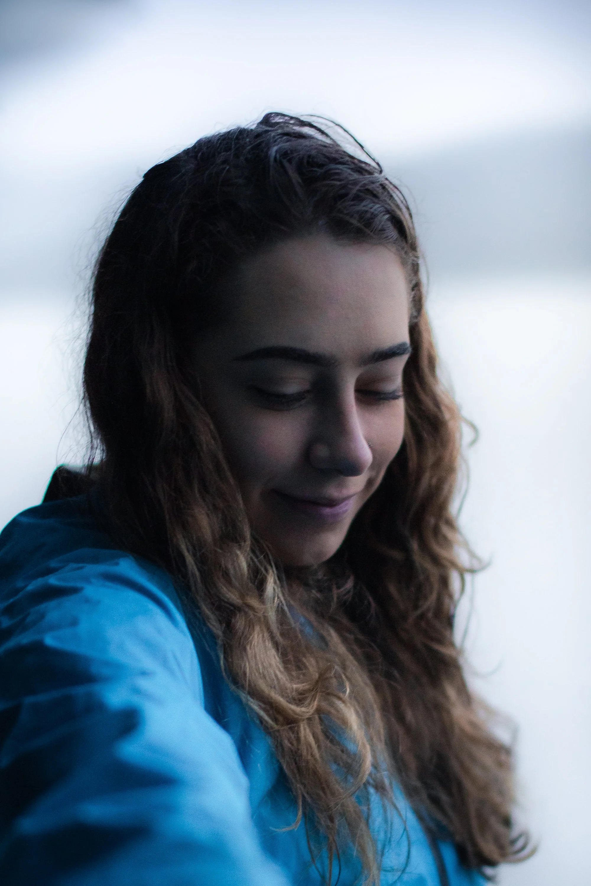 Man in white shirt and khaki pants standing on rocks near the water, looking down. Portrait by Archie Carmel.