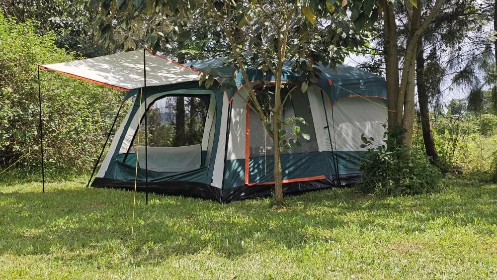 A camping tent set up on a grassy field, with trees and bushes nearby.