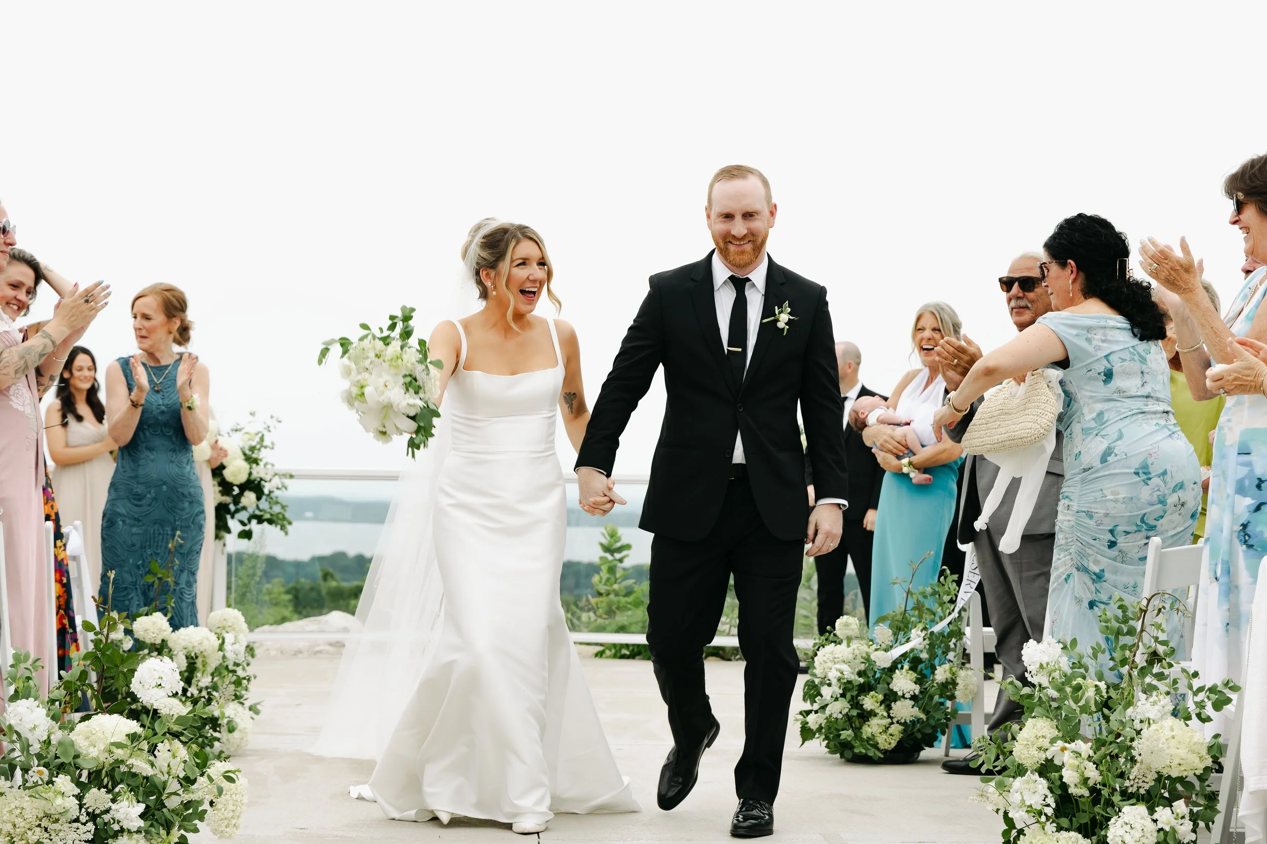 Newlyweds walking down the aisle surrounded by lush white and green seasonal wedding flowers