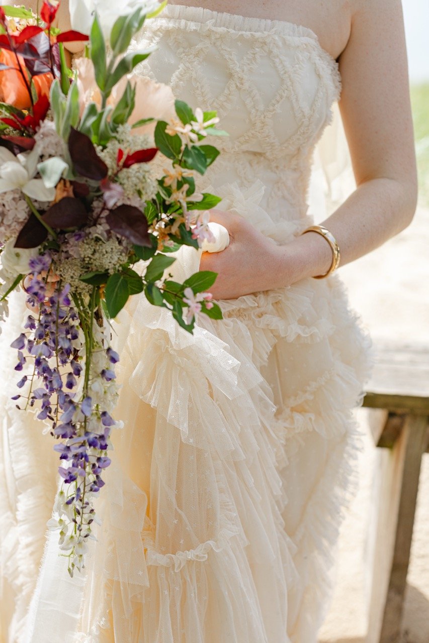 Close-up of the bride holding a cascading seasonal wedding bouquet with purple wisteria, peach flowers, burgundy foliage & greenery at Watervale Inn.