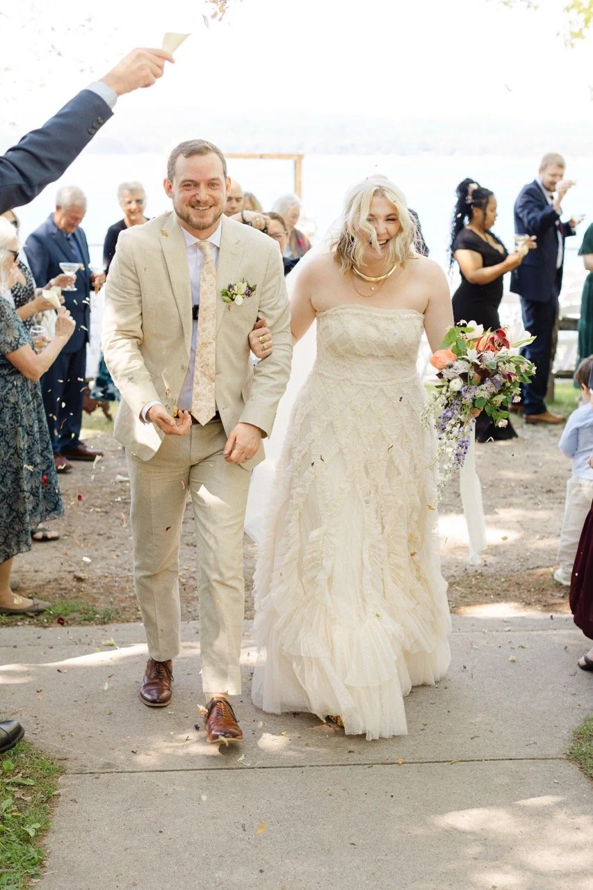 Nell and Evan smile as guests toss colorful dried flower confetti during their wedding recessional at Watervale Inn.