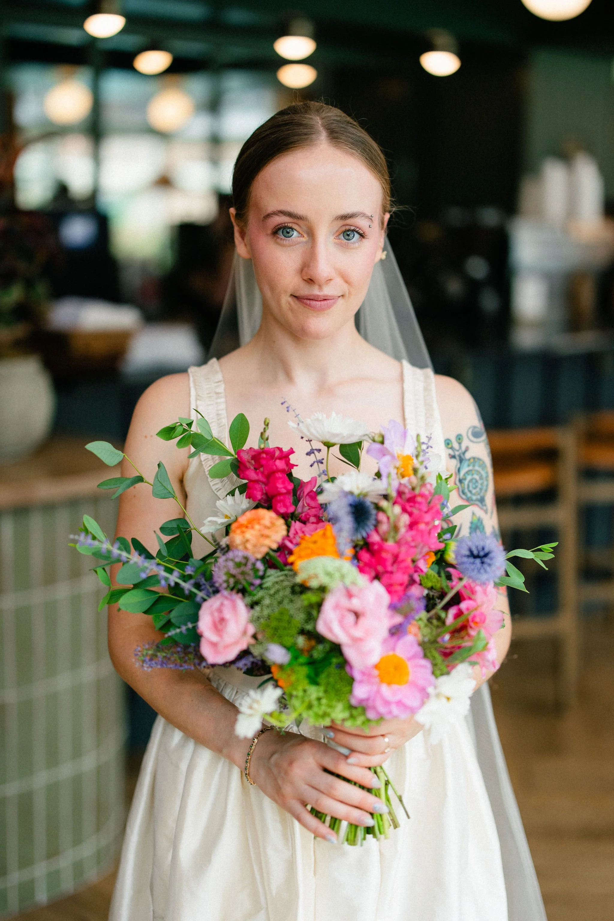 Bride holding bright, colorful bridal bouquet with pink, orange, and purple seasonal flowers indoors