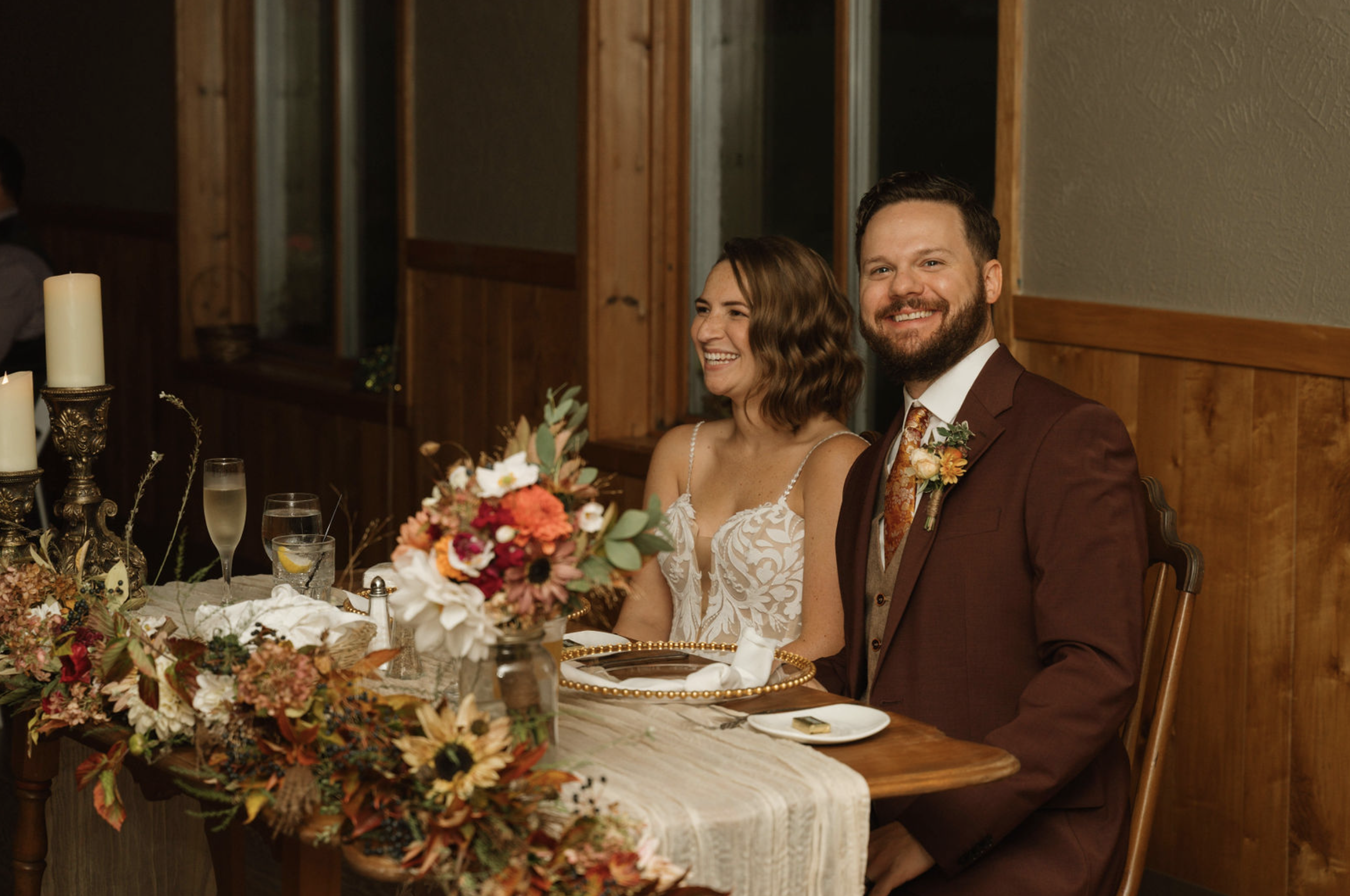 Sweetheart table with fall wedding flowers, textured linens, and candlelight creating an intimate reception setting