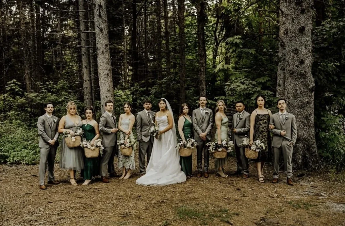 Wedding party poses among tall trees with attendants carrying seasonal flowers in woven baskets and handheld arrangements.