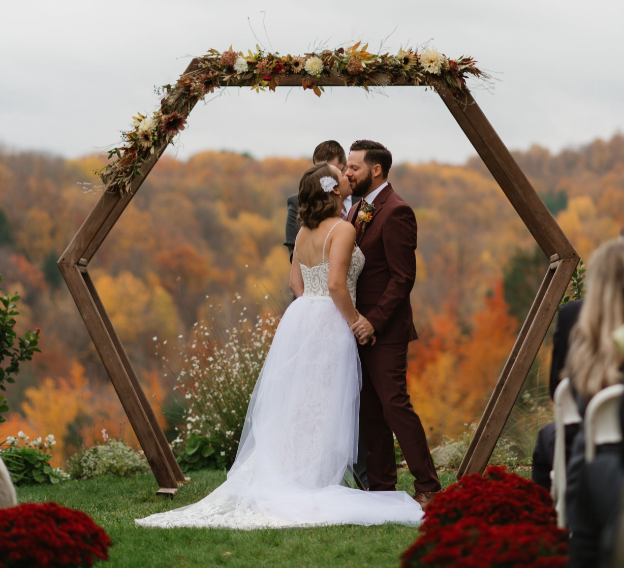 Outdoor fall wedding ceremony with hexagonal wooden arch and seasonal floral installation overlooking colorful Northern Michigan landscape
