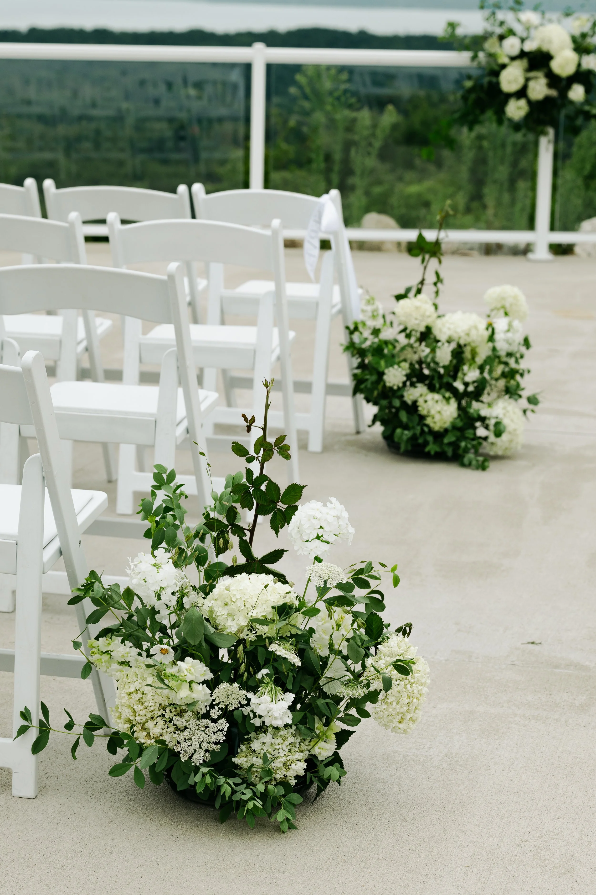 White hydrangea and greenery wedding arrangements lining the ceremony aisle with scenic Northern Michigan views