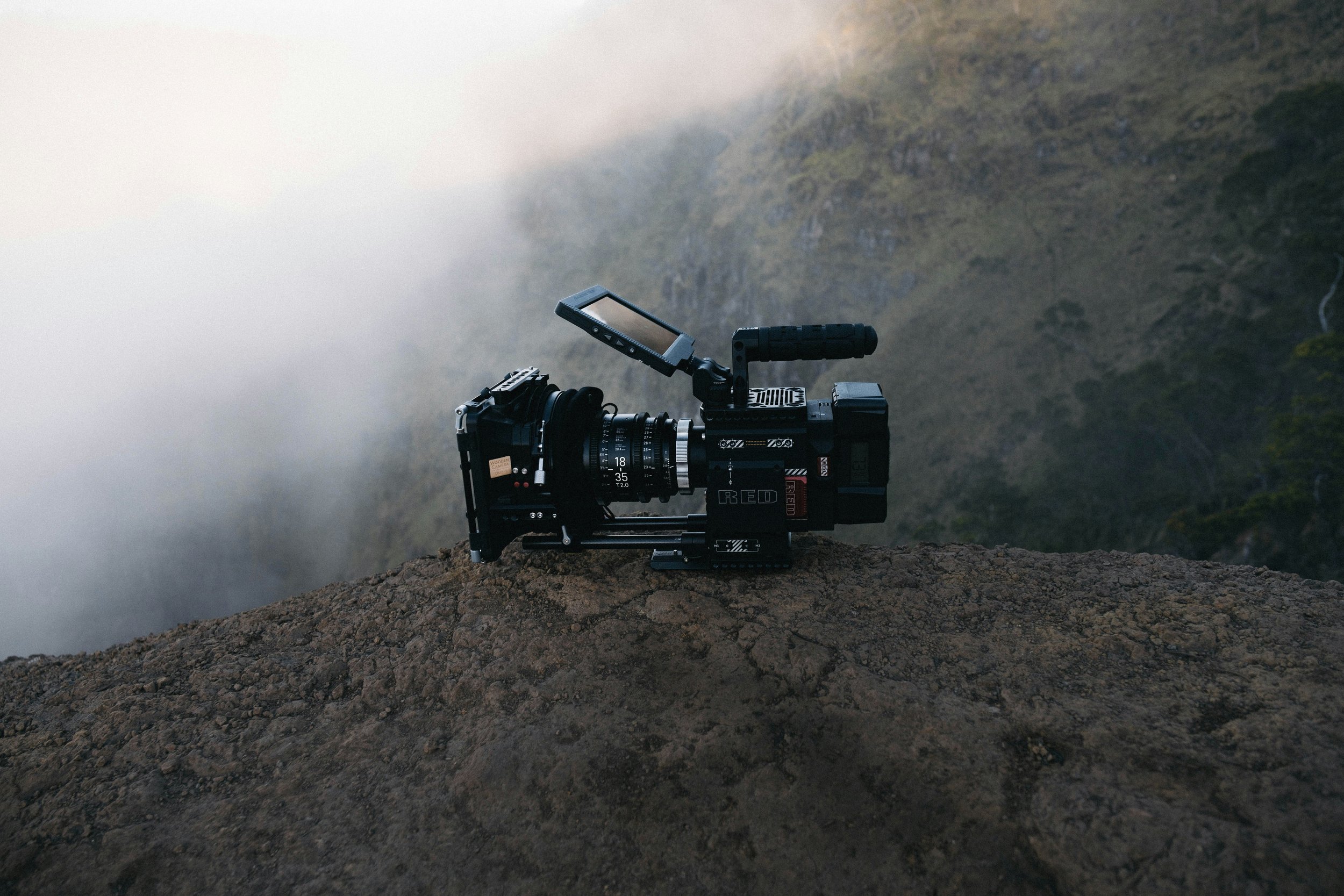 Une caméra professionnelle sur un terrain rocheux au sommet d'une montagne, entourée de brouillard, avec une vue sur des montagnes en arrière-plan.
