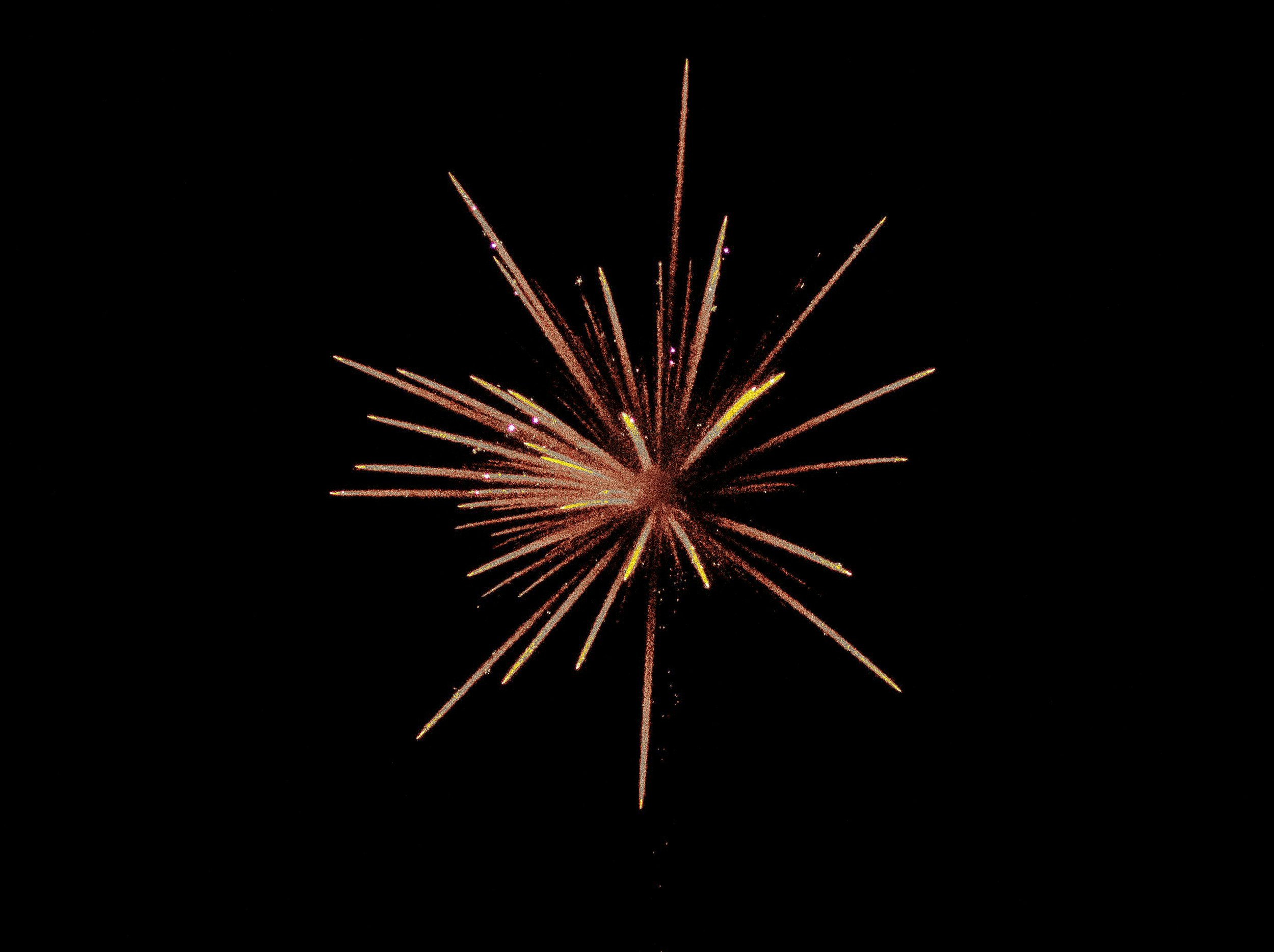 Un feu d'artifice éclate dans le ciel noir, avec des rayons lumineux dorés et teintés de rose.