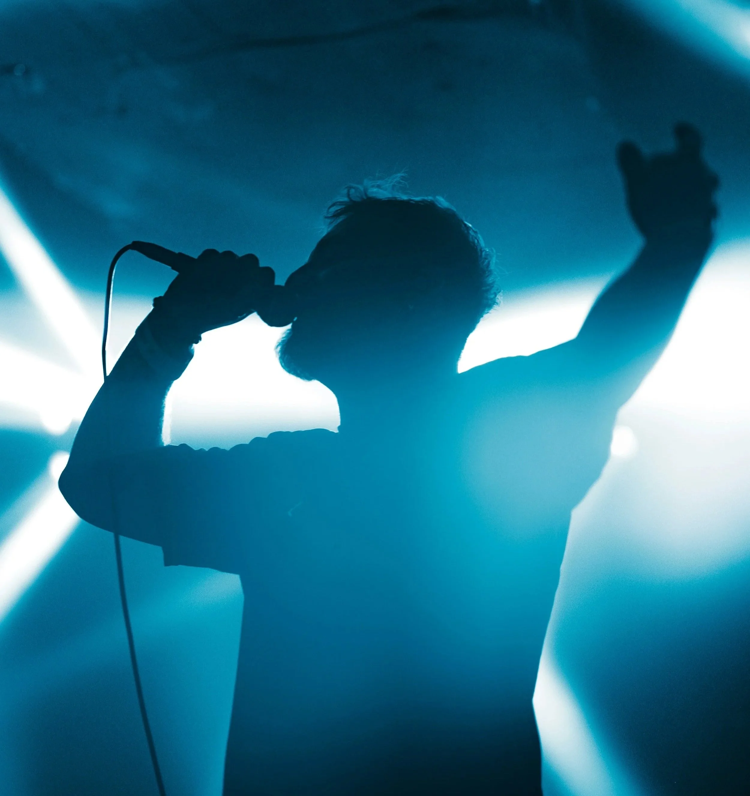 Silhouette d'un chanteur ou musicien lors d'une performance, tenant un microphone et levant la main, éclairé par une lumière bleue en arrière-plan.