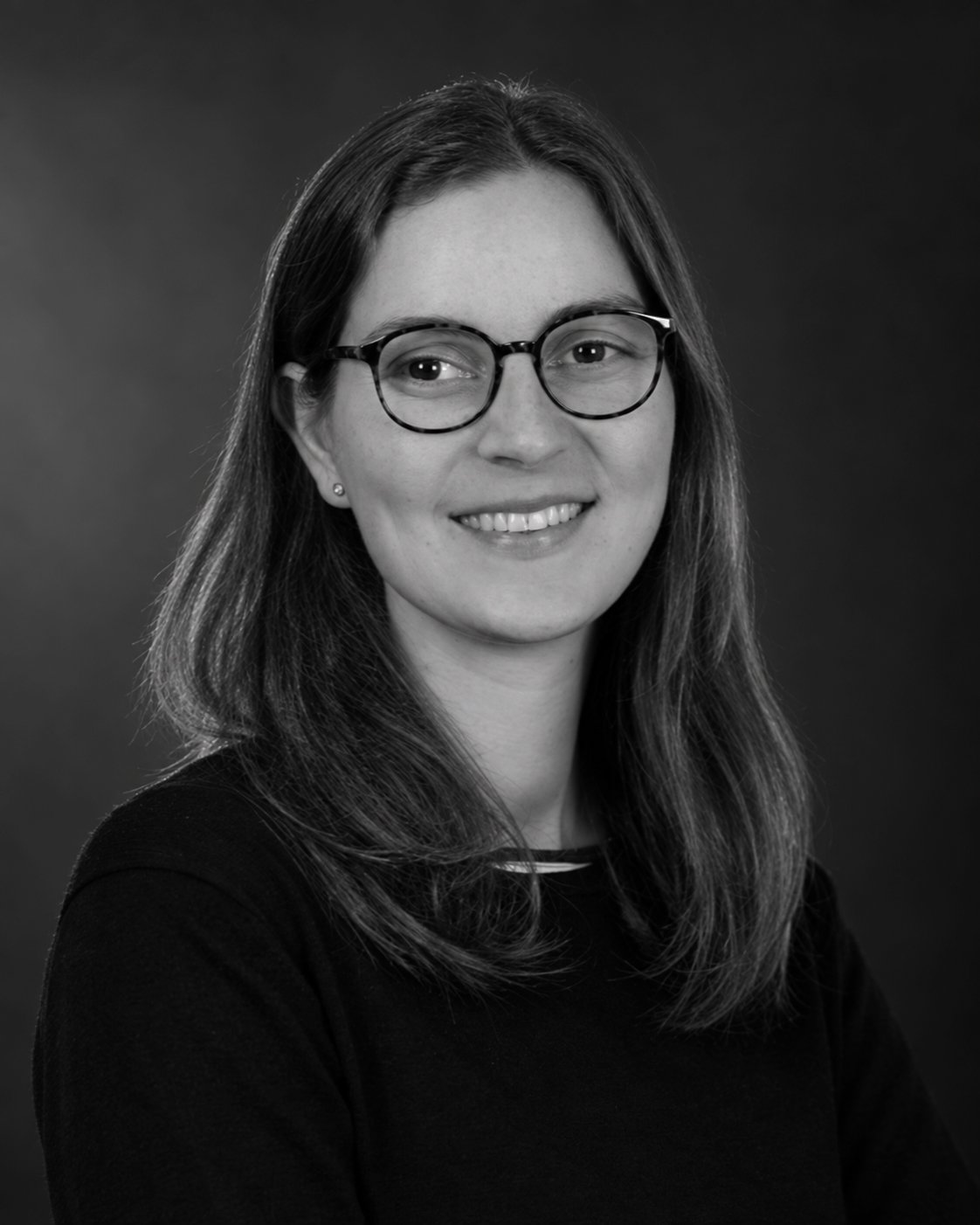 A young woman with shoulder-length hair, glasses, and a black top, smiling at the camera.