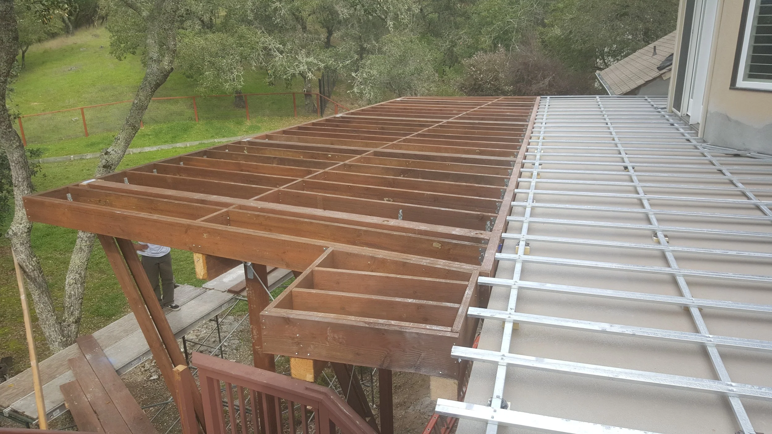 Hybrid deck frame over a living area with pressure treated wood joists and aluminum sub-framing prepared for waterproofing.