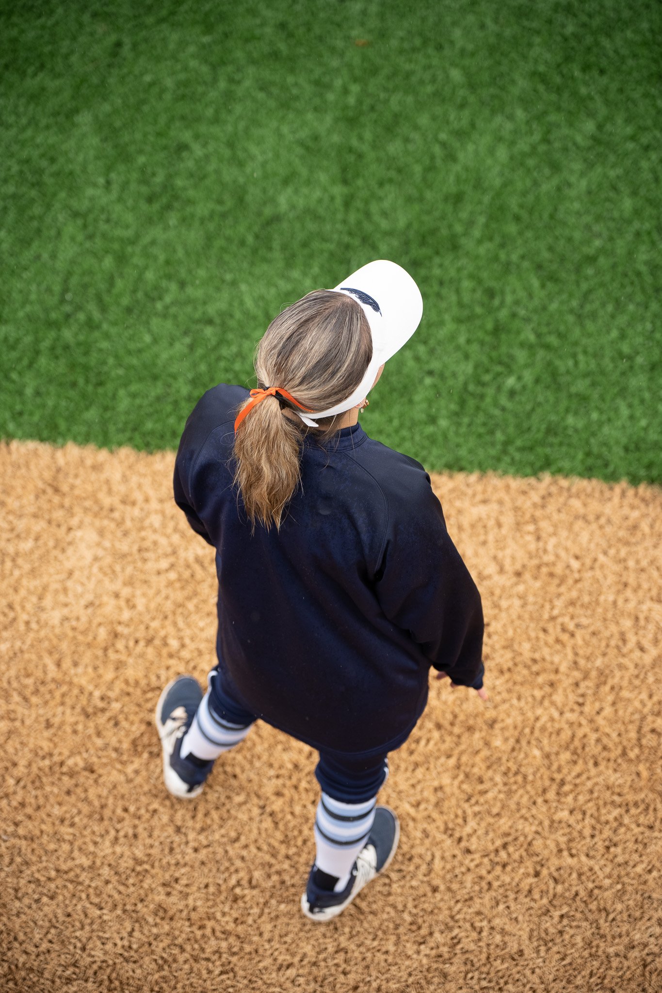 Person wearing a white cap, navy jacket, and striped leggings walking on a turf field.