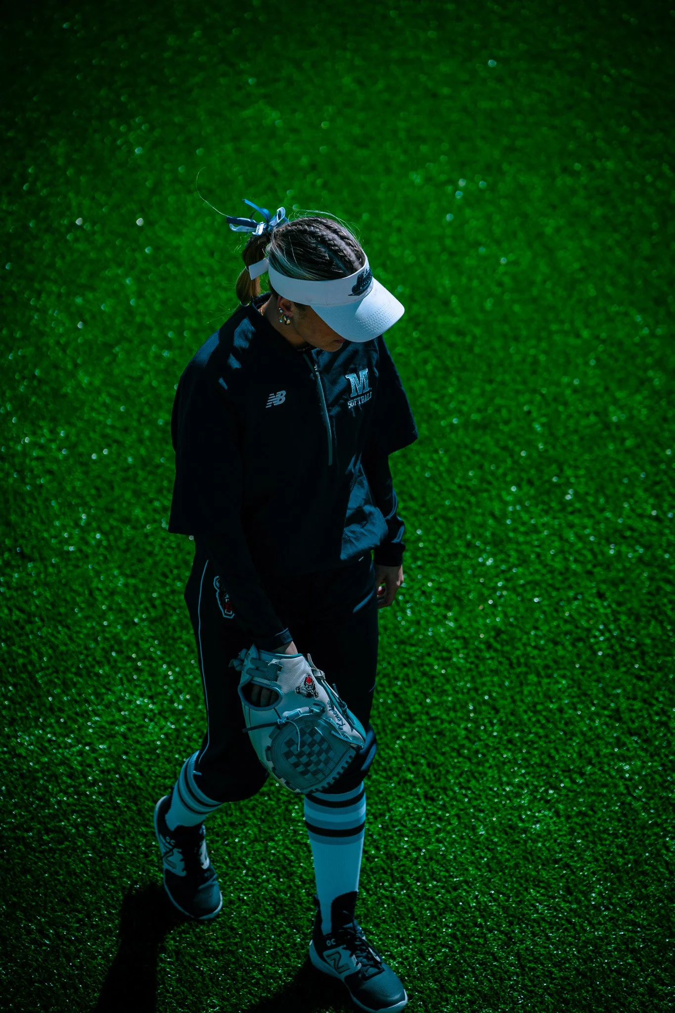 A person wearing a sports uniform with a visor and holding a baseball glove, standing on a green field.