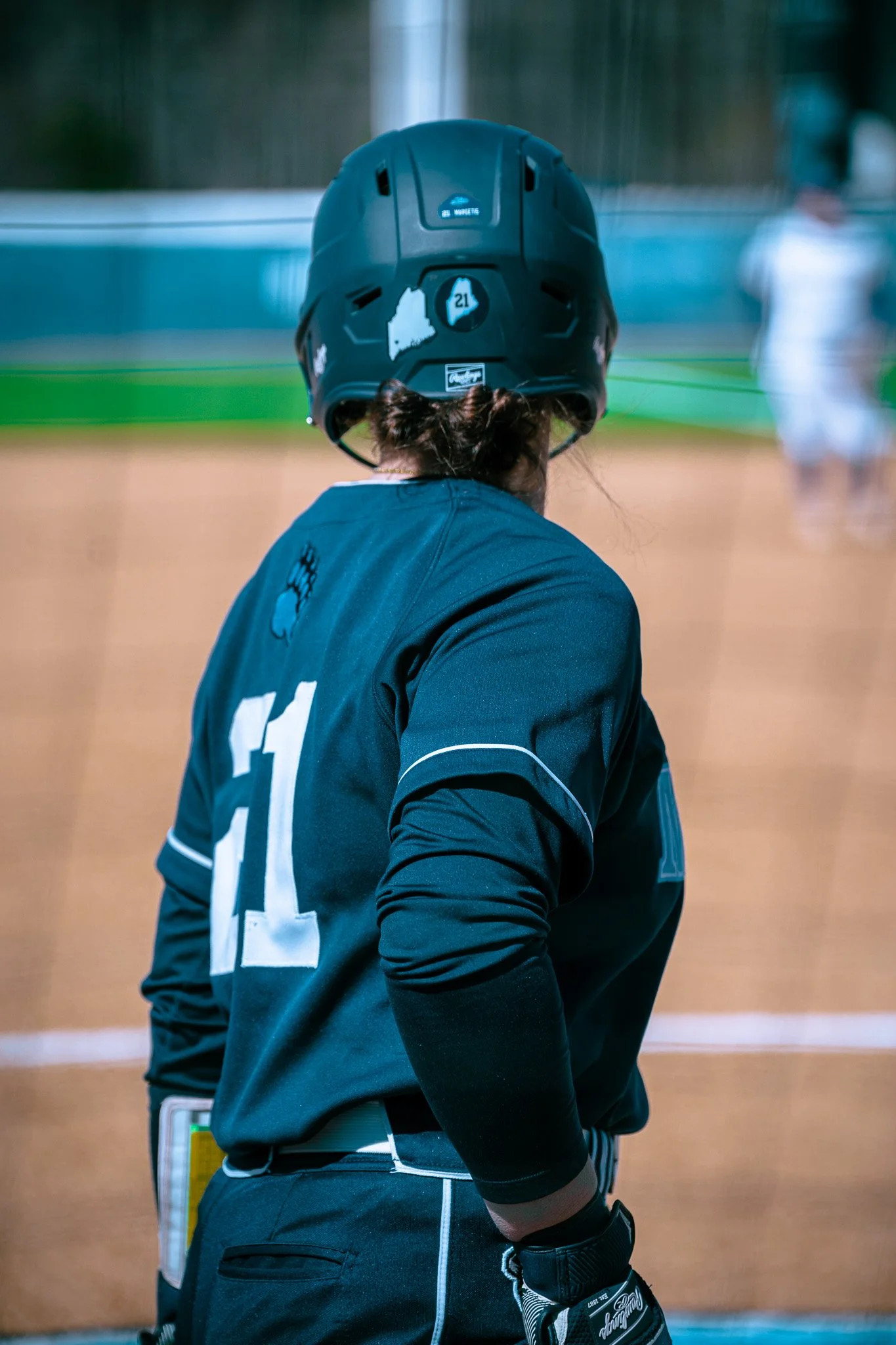 Softball player in black uniform and helmet, number 21, standing on field