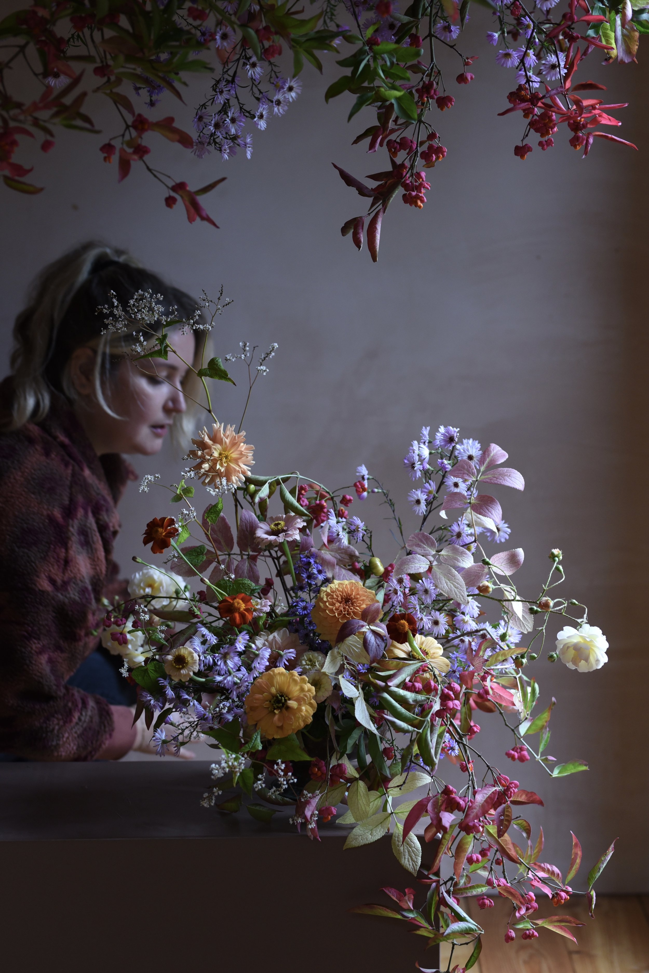 A woman arranging a large bouquet of colorful flowers with hanging blossoms above her.