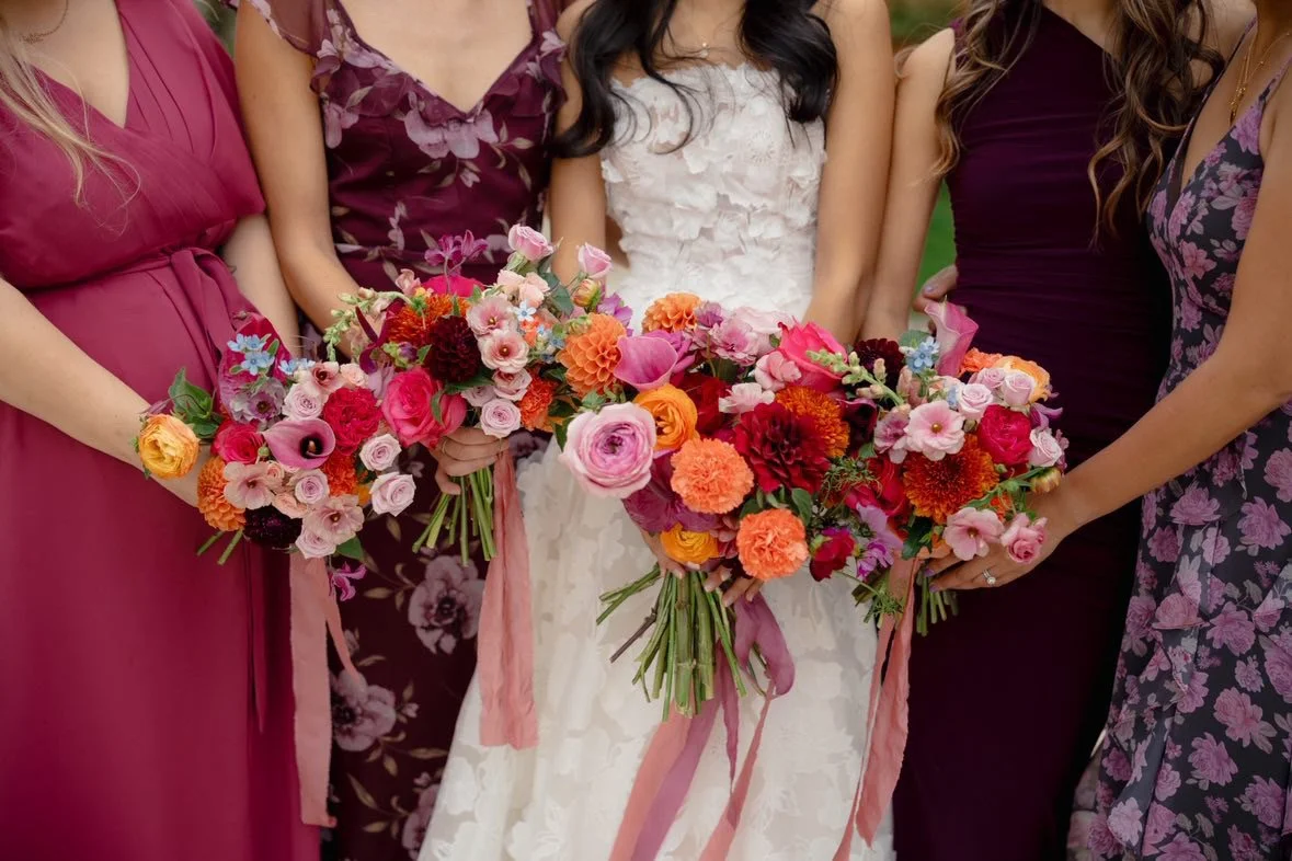 Group of women holding colorful floral bouquets at a celebration or wedding.