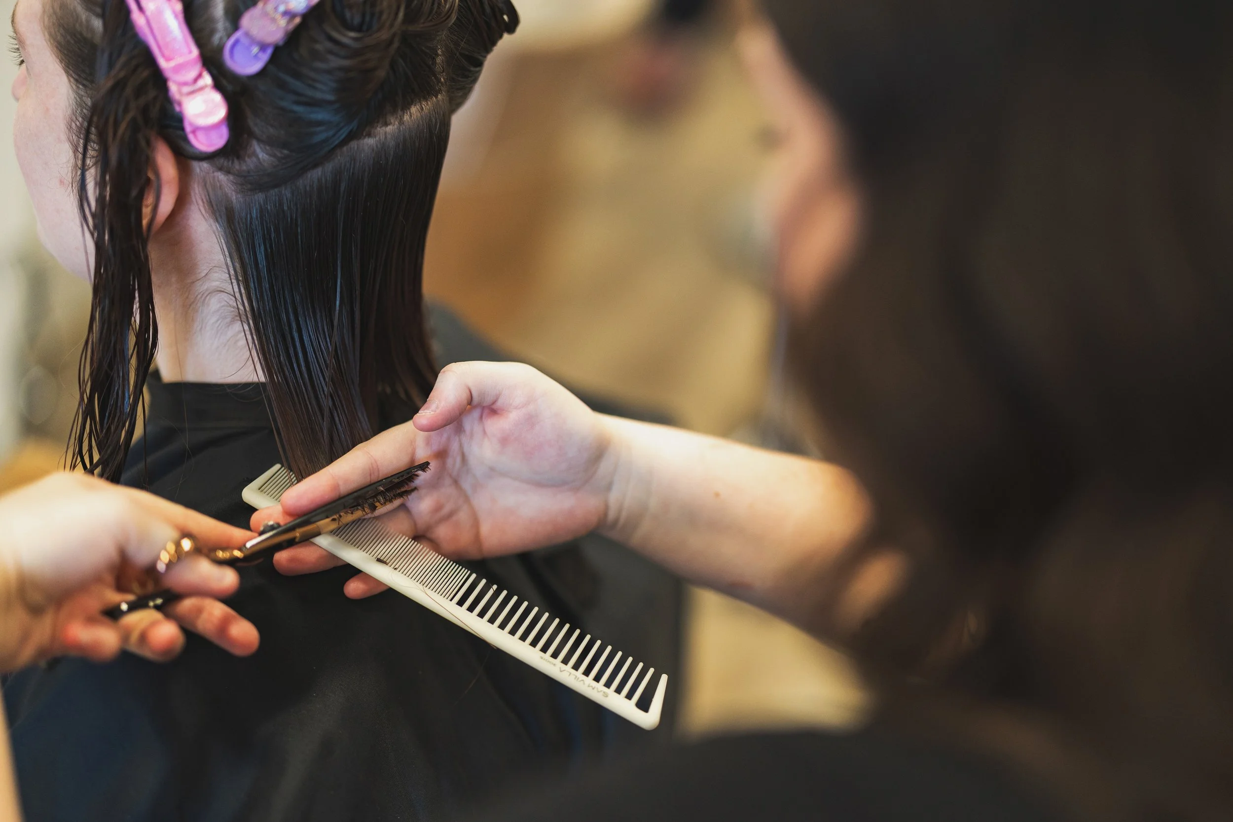 A hairstylist cutting a client's dark, wet hair with scissors, using a comb at a salon.