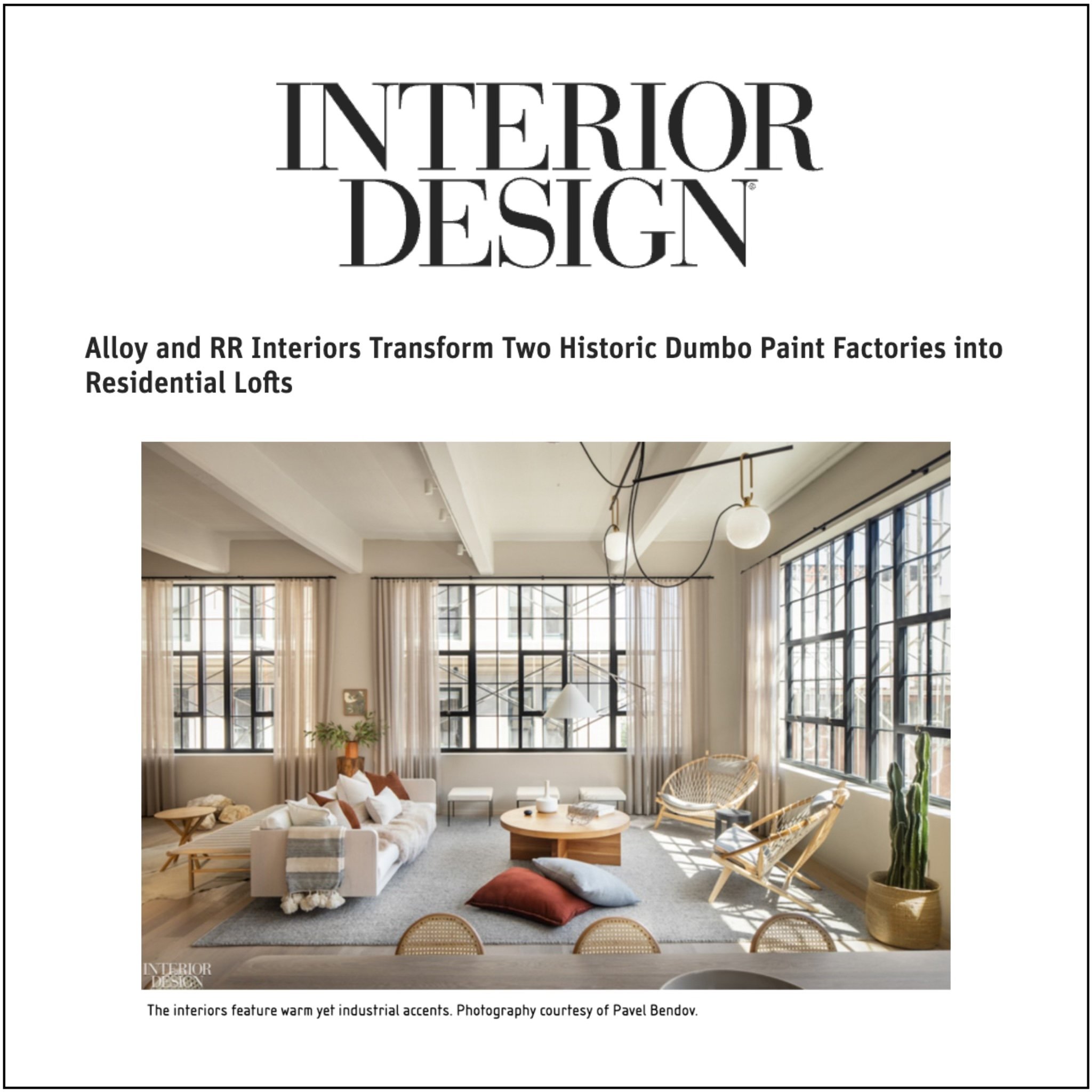 A modern living room with large grid windows, white walls, ceiling beams, and industrial-style light fixtures. The room features a white sofa, various pillows, a round wooden coffee table, wicker chairs, a cactus plant, and sunlight streaming through the windows.