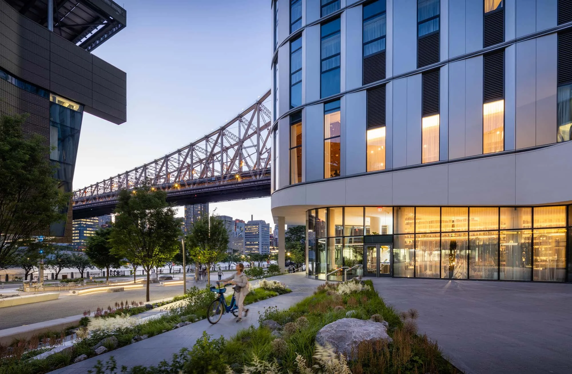 Graduate Roosevelt Island Hotel surrounded by trees, with a bridge in the background, designed by Snohetta in New York