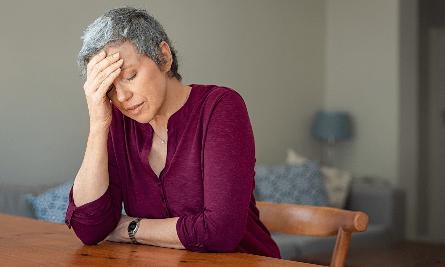 A woman sitting at a table, stressed and holding her head.